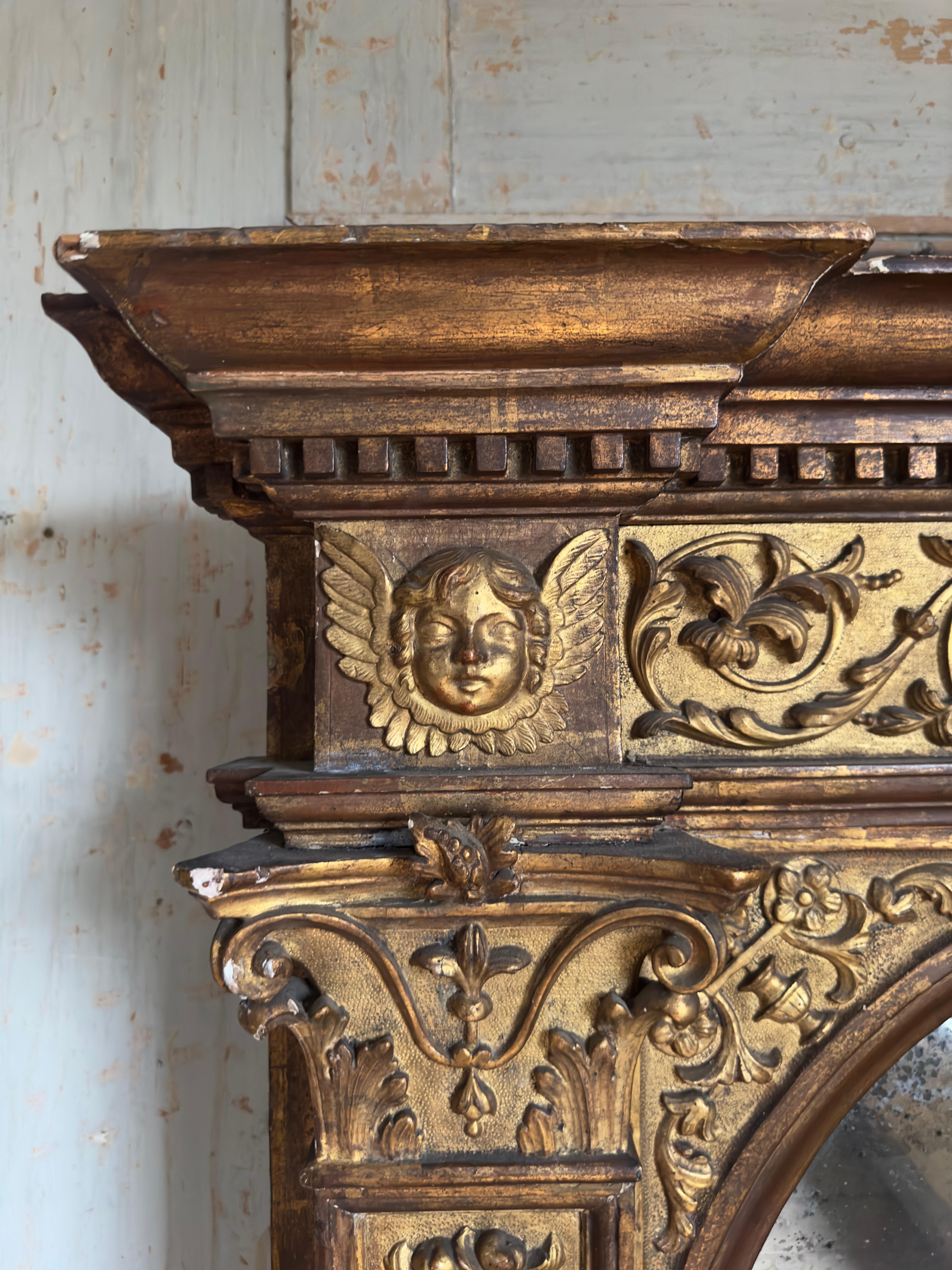 Grand et imposant miroir en bois doré et gesso sculpté italien du 19e siècle ou plus ancien. Dans le goût maniériste et de forme tabernacle. L'arc central avec des plaques fendues, flanqué de pilastres classiques. La corniche dentelée moulurée