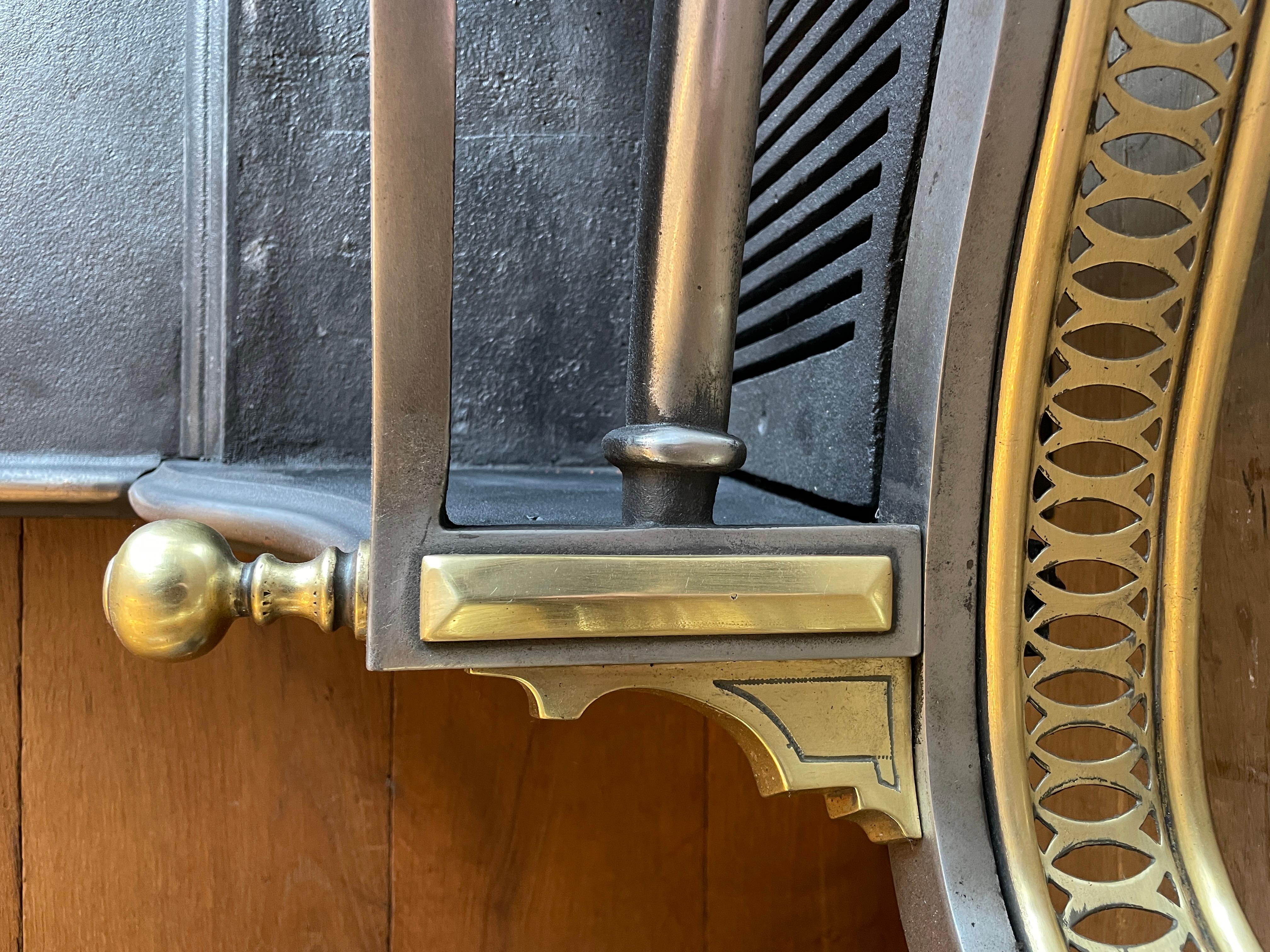 A large English late 19th turn of the 20th century fire grate. The front legs in brass with splayed feet supporting large bulbus baluster finials. The cut fret in geometric form beneath a bowed burning area, caped with spherical finials, lozenge