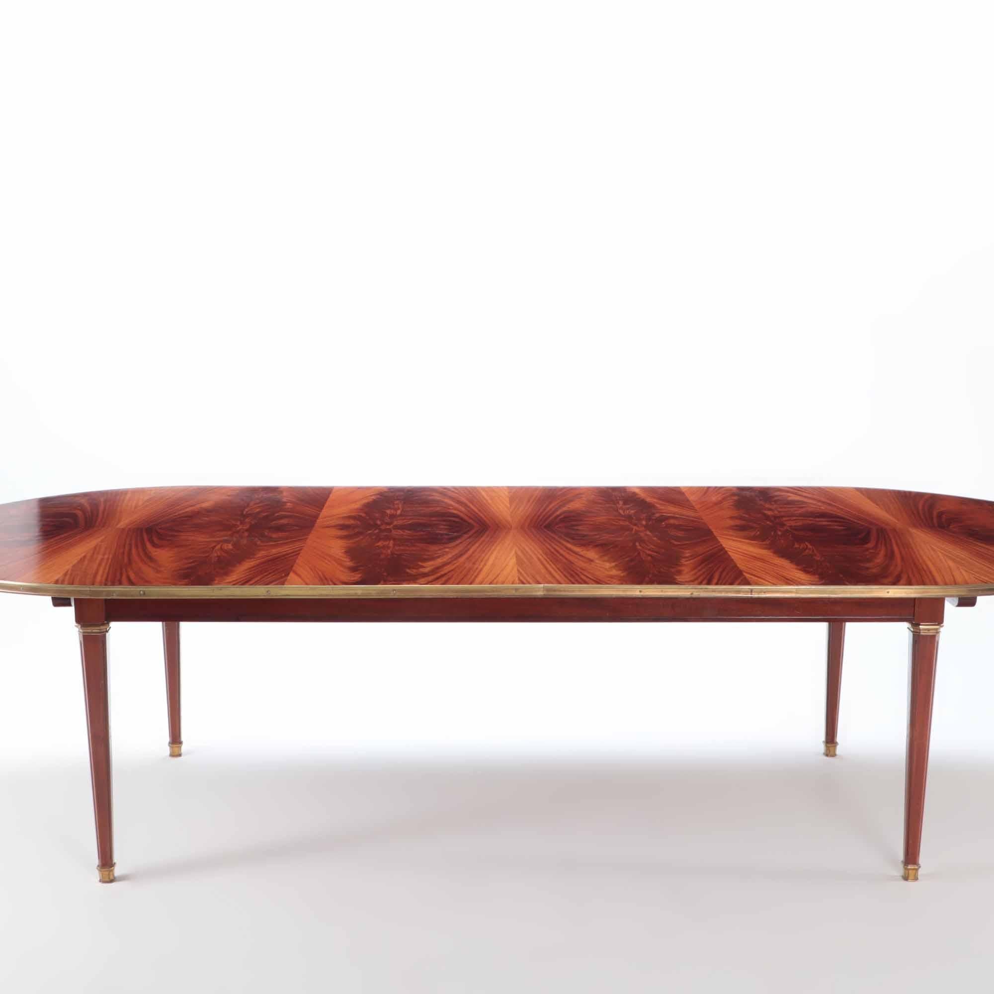 A French Flame mahogany dining table with bronze trim attributed to Jansen. Has two leaves with fall down legs for additional support. Square tapering legs ending in brass sabots. circa 1945. Each leaf is 30