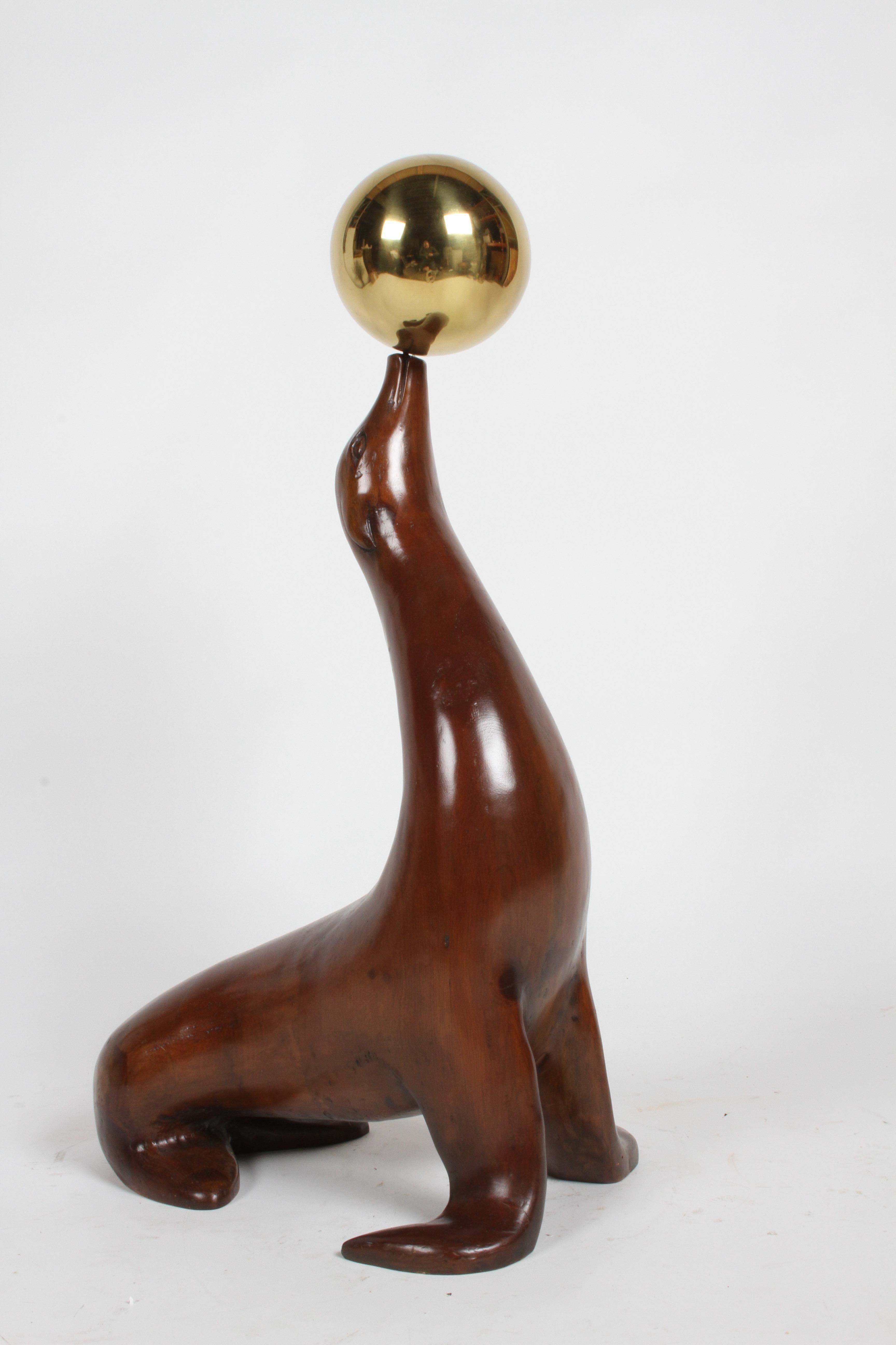 Straight out of an interior from the exuberance, glam and high style days of 1970s. This large scale vintage English sculpture of a sea lion or seal is carved out of elmwood, balancing a large brass ball on his nose. A rare find, in very nice
