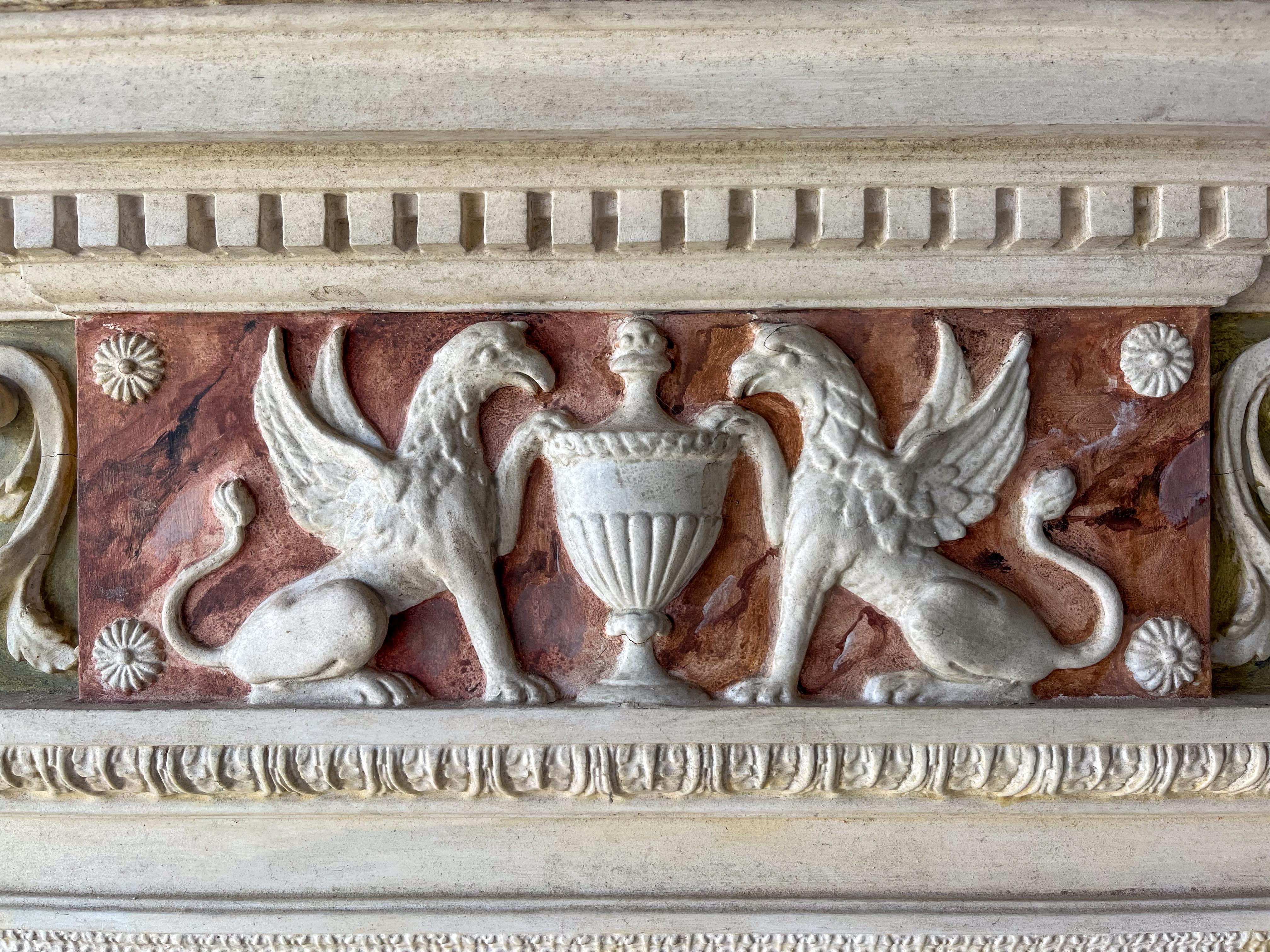 Une grande cheminée sculptée à la main et en gesso avec un manteau, des colonnes et une frise en faux marbre peint. La plaque centrale est ornée d'une urne d'Adams et de détails feuillagés. La frise au-dessus du miroir est ornée de griffons, d'urnes