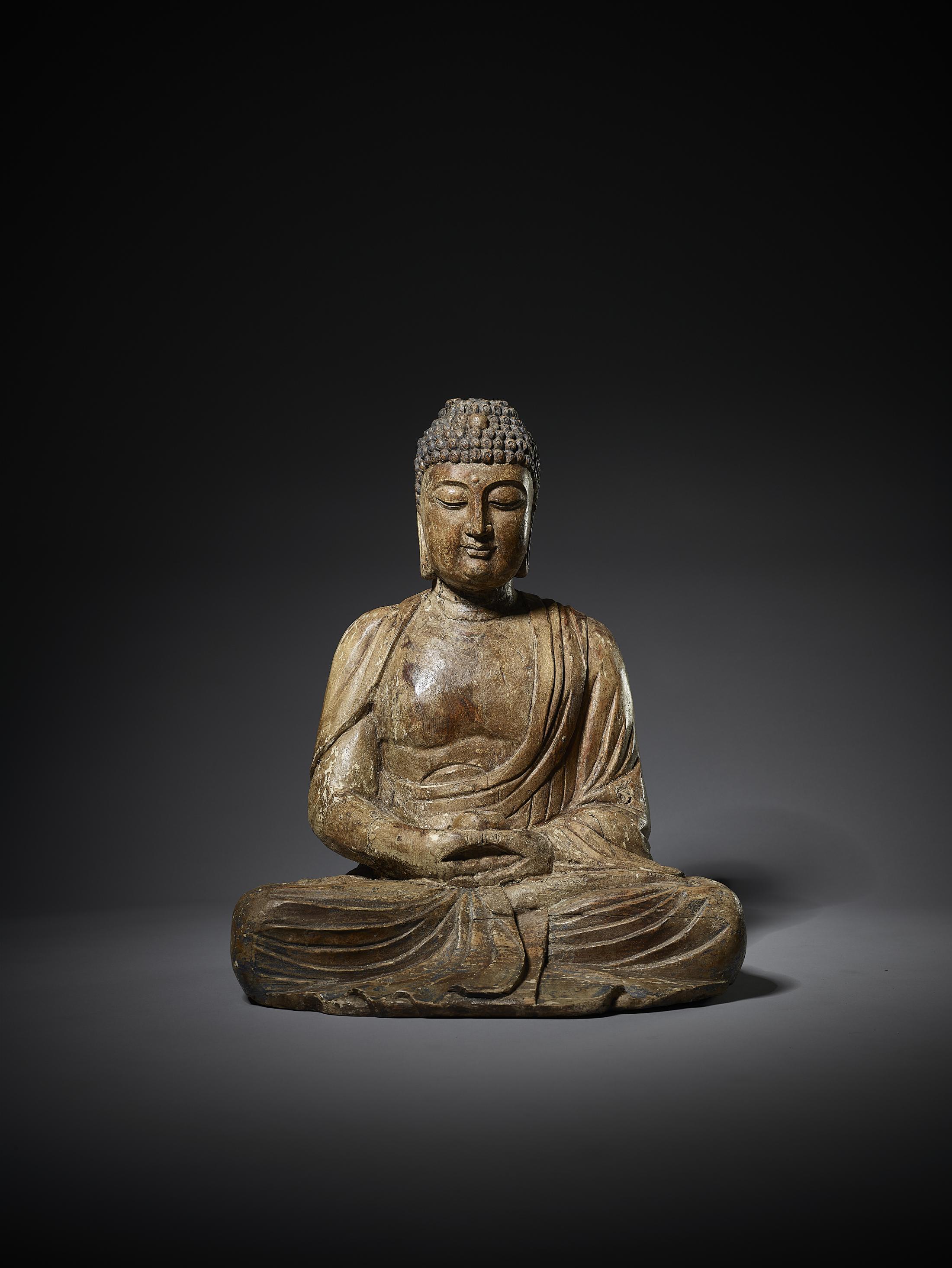 A LARGE CARVED WOODEN FIGURE OF BUDDHA, MING DYNASTY （1368-1644）

China, 1368-1644. Seated in dhyanasana, the arms lowered in dhyanamudra, holding an alms bowl, wearing long robes falling into voluminous folds and opening at the chest, the face with