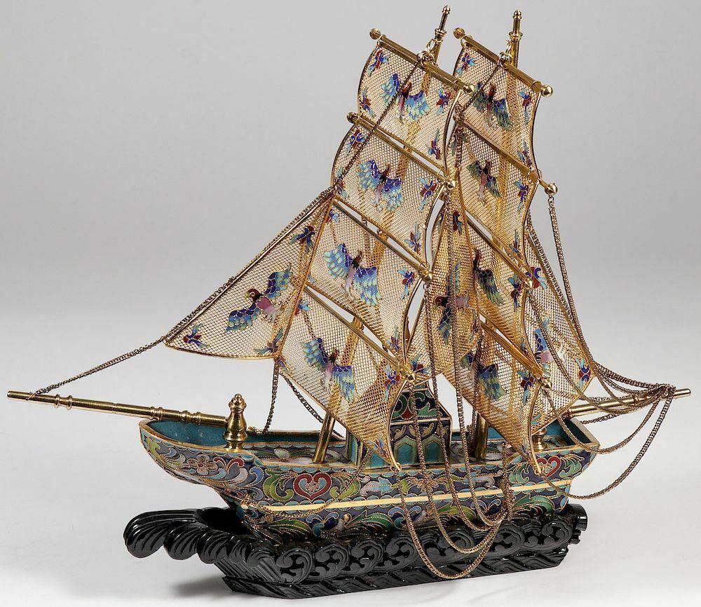 A Large Chinese 
Cloisonne Enamel Filigree 
and Gilt Boat with Wood Base 
 
The sails with colorful enameled birds, resting on a conforming carved wood base. Overall length 18 inches (46 cm).

Condition: excellent condition with some age