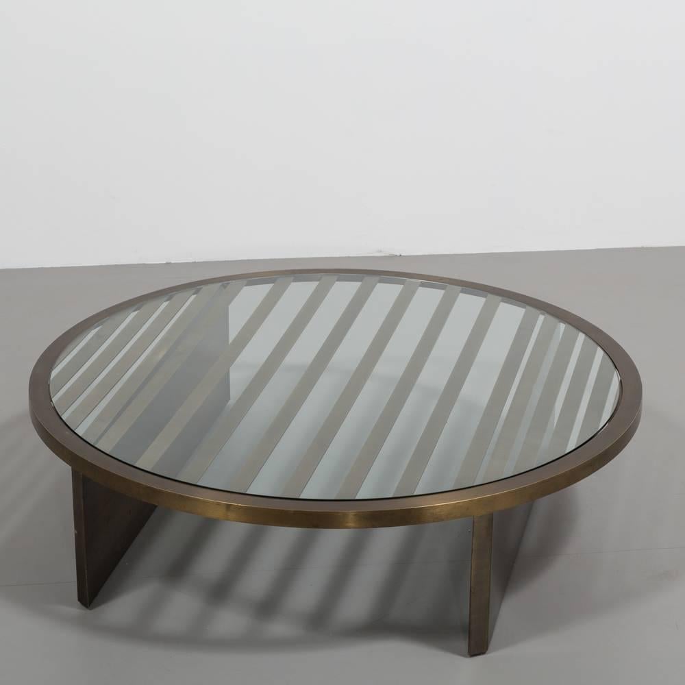 A large circular bronze framed coffee table with glass top, 1980s 
The graphic pattern of graduated slats punctuated by the bold legs are really interesting details on this table and strongly sets it apart. The bronze has a great depth in tone and