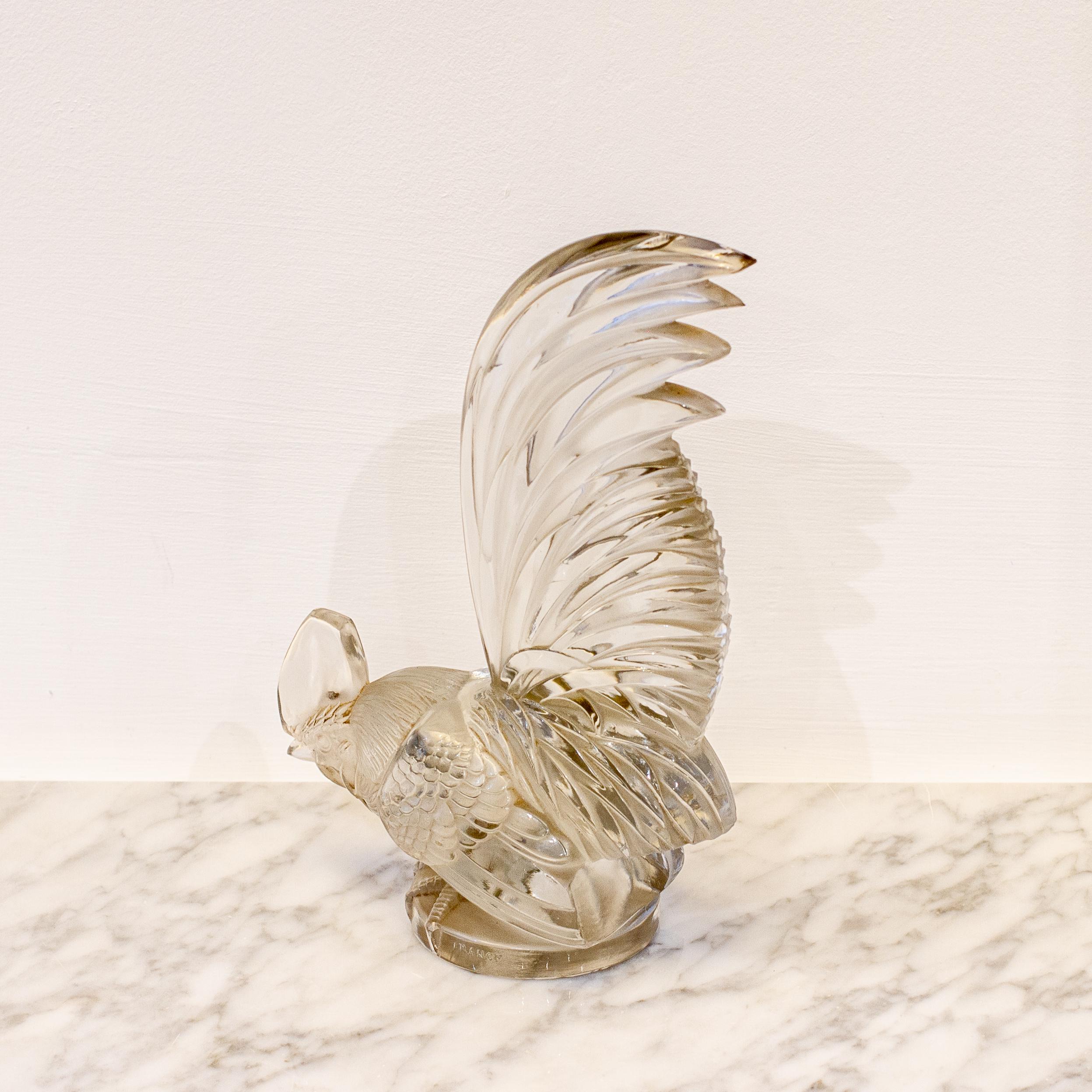 A large clear glass rooster car mascot titled 'Coq Nain' by René Lalique, model number 1135, circa 1928.

René Lalique (1860-1945) was a French jeweller whose glass works of art contributed significantly to the art nouveau movement. His jewellery