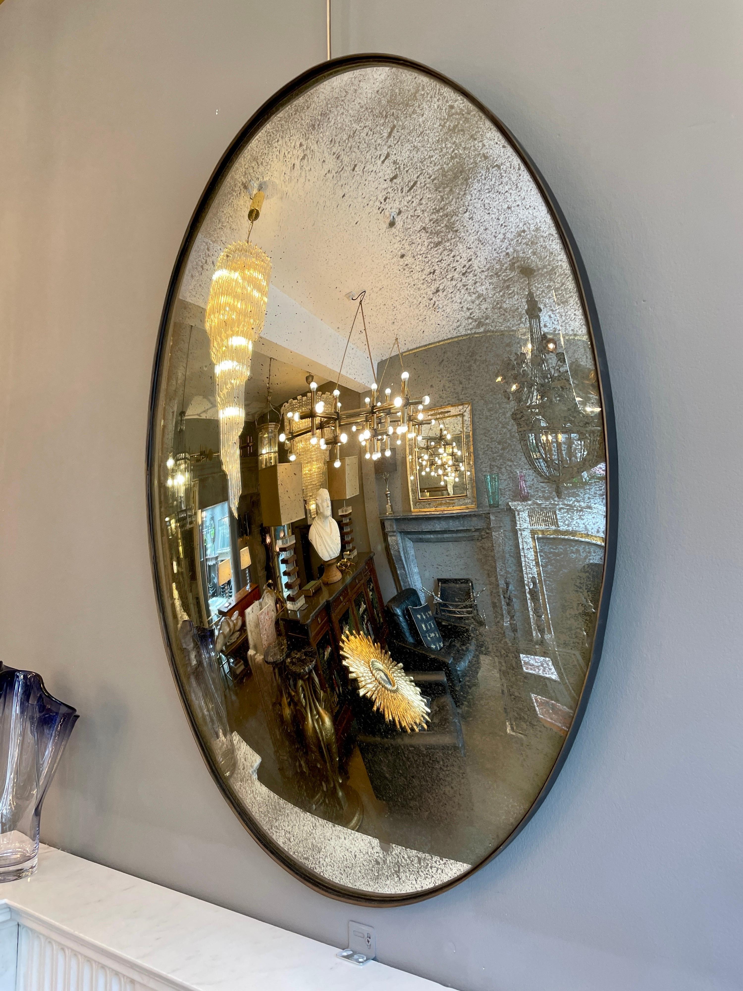 An oval shaped distressed convex mirror with bronze finish banded frame.