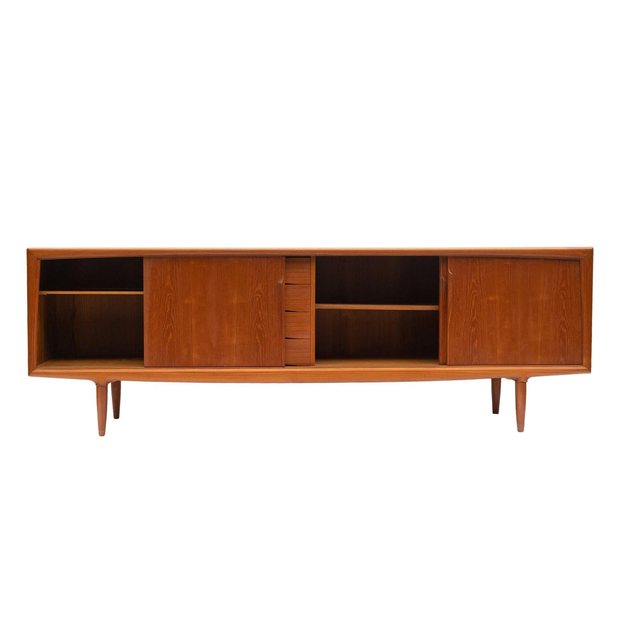 A Large Danish Modern teak sideboard designed by Gunni Omann for Aco Møbler, with three sliding doors and a bank of four fitted drawers, with organically sculpted pulls, on a shaped base with round tapering legs; finished on all four sides, Denmark,