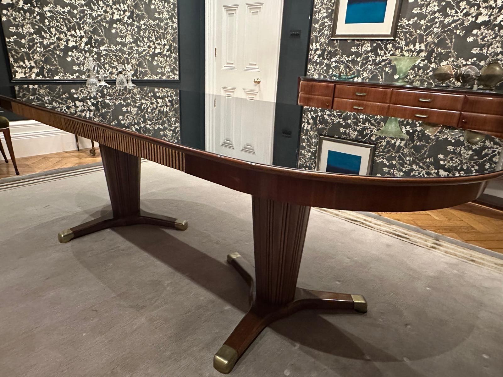 Extraordinaire table de salle à manger conçue par Melchiore Bega dans les années 1950, en merisier foncé et plateau en verre noir avec détails dorés, reposant sur deux bases cannelées avec pieds en laiton. 
La table a été entièrement restaurée par