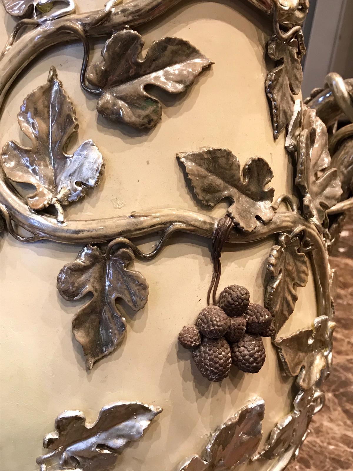 Of a baluster form with a flaring neck with a beaded design, the vase is made of a buff coloured stoneware, covered with a vine, leaf and berry motif that also forms two low handles. The latter is covered with silver overlay.

Dimensions: Height 75