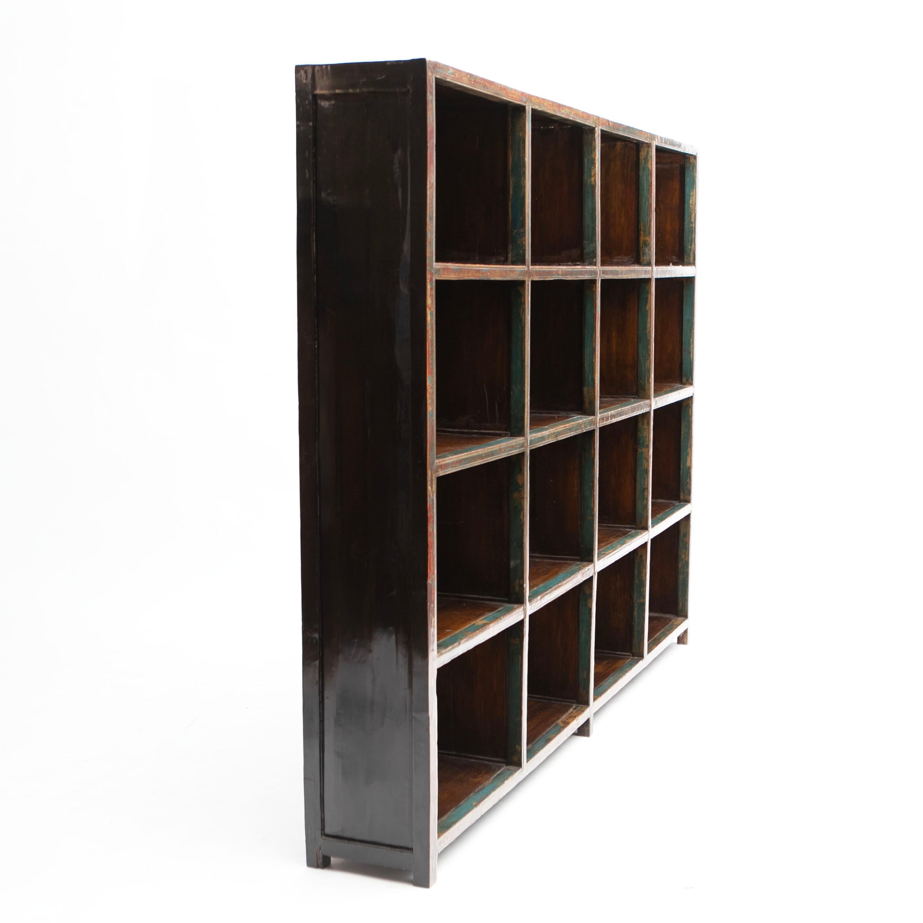 A large early 20th-century elm wood bookcase from China.
This piece features 16 square cubbies (4x4) doubling as shelves.

The lacquer displays a charming age-related patina, with black lacquer on the sides and polychrome lacquer on the front.
(Is