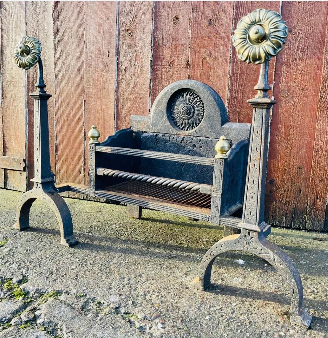 A unique and elegant large early cast iron and brass Scottish Arts & Crafts fire grate basket in the Lorimer manner. An arched shape fire back inset with a stylized sunflower, the three bar fire front showing a central rope effect design to the bar,