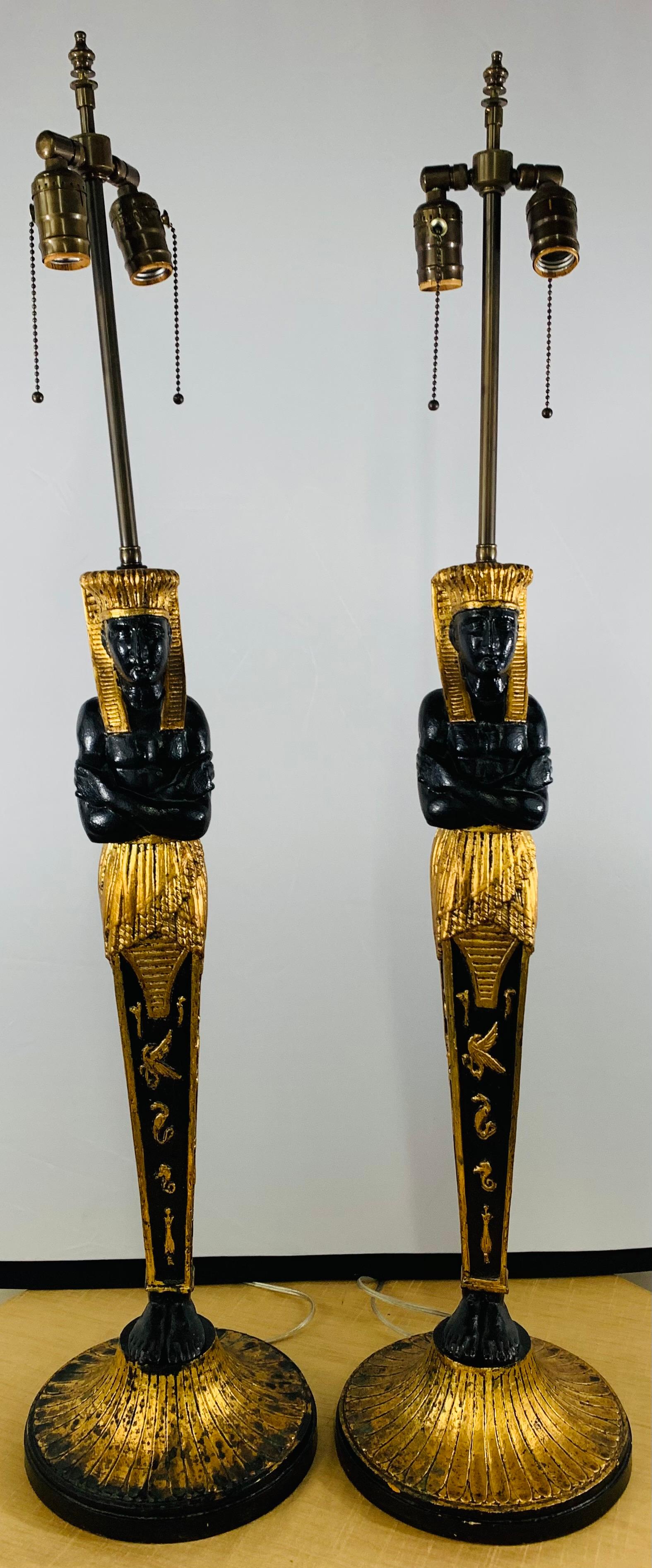 A stunning 1970s pair of ebonized table lamps in the shape of Pharaoh finely hand carved and gild decorated. The black and gold Pharaoh lamps features amazing details and Amarna letters ( Ancient Egyptian letters). Each lamp has two standard bulbs