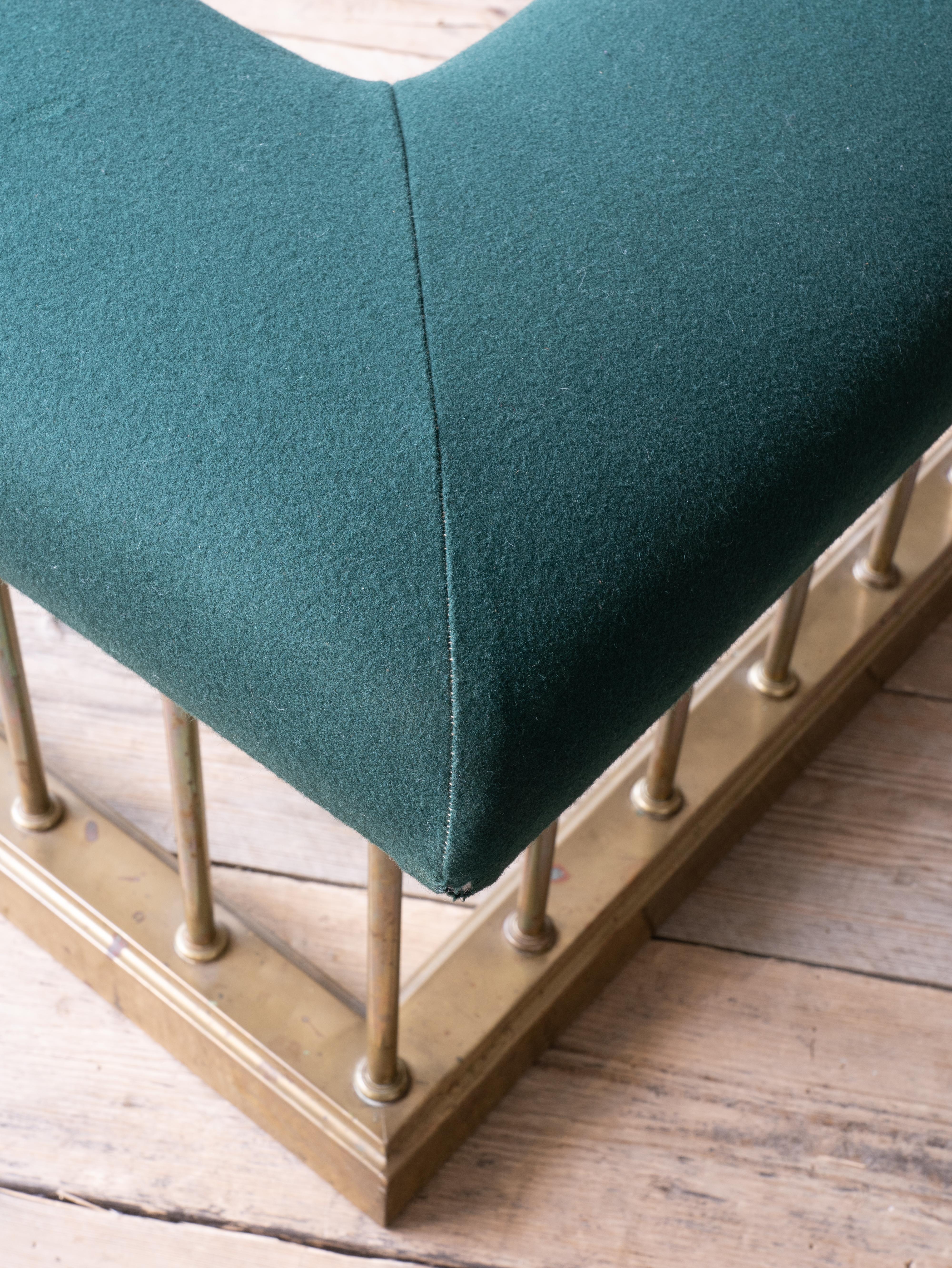 A large brass club fender with a wide seat upholstered in green baize.

