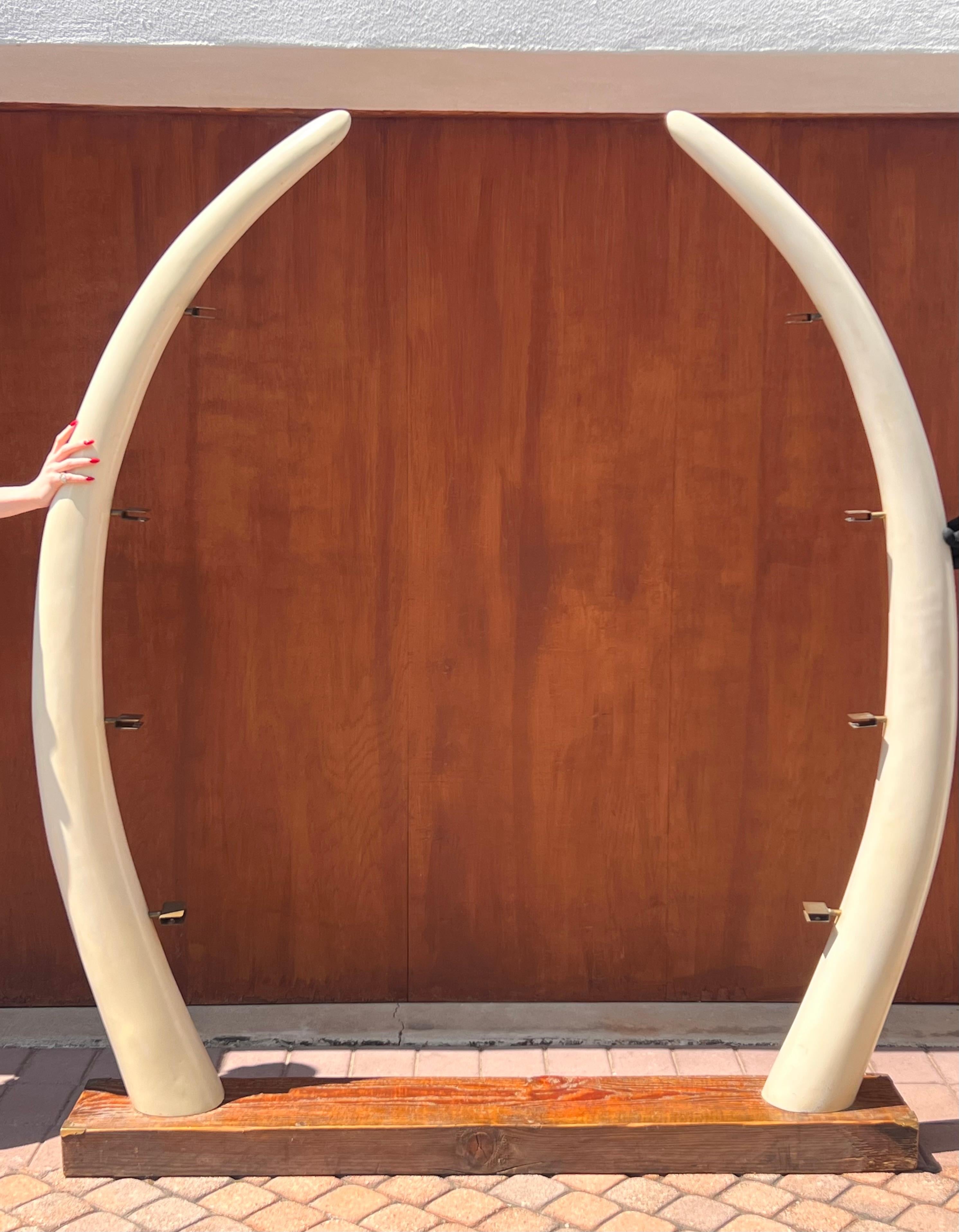 An absolutely stunning mid century étagère featuring a tropical wood base, resin elephant tusks, metal hardware, and glass shelves, circa 1960s. This piece is an incredibly unique relic from the mid century modern era that relished tropical and