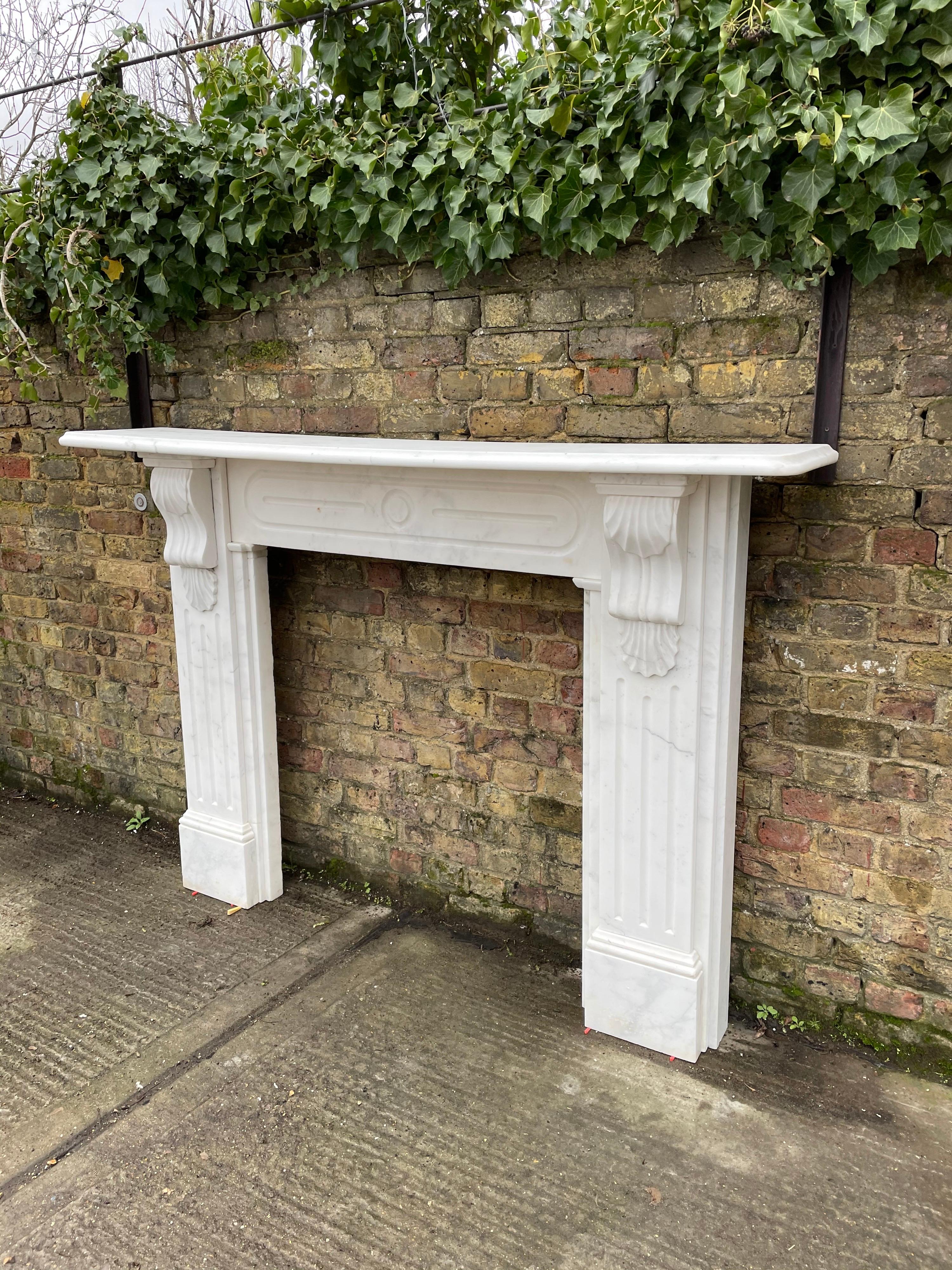 A large 19th century Italian white marble fireplace from the Victorian period. The fluted jambs with double shell Corble brackets supporting a large generous Ogee moulded shelf and fluted circular motif frieze. Quality Italian white marble with