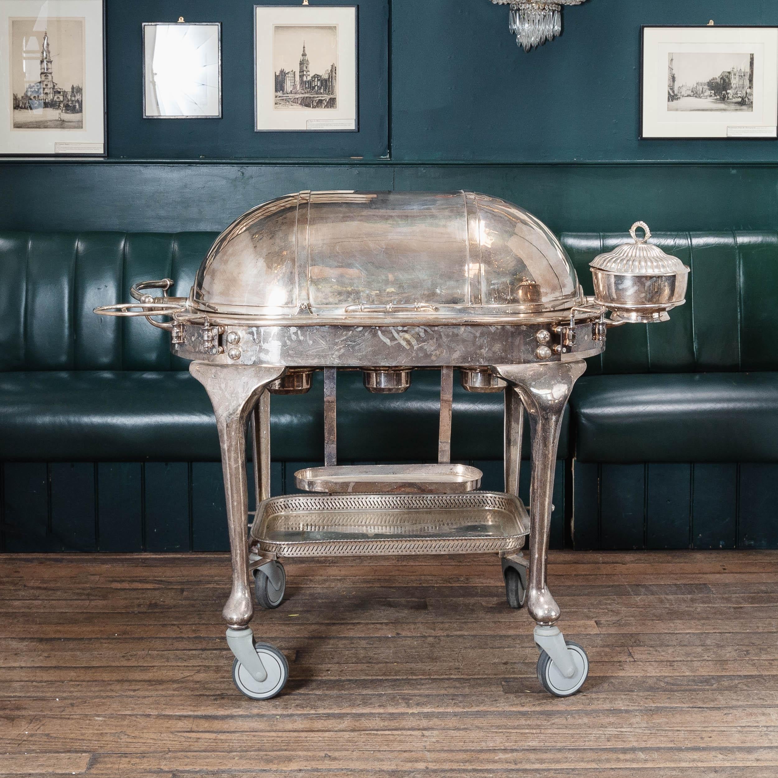 An early twentieth century large silver plated beef trolley with hallmark to the underside for 'James Deakin & Sons Ltd' of Sheffield, the roll-top lid opening to reveal carving board and three sauce vessels,  with three oil burners below, all