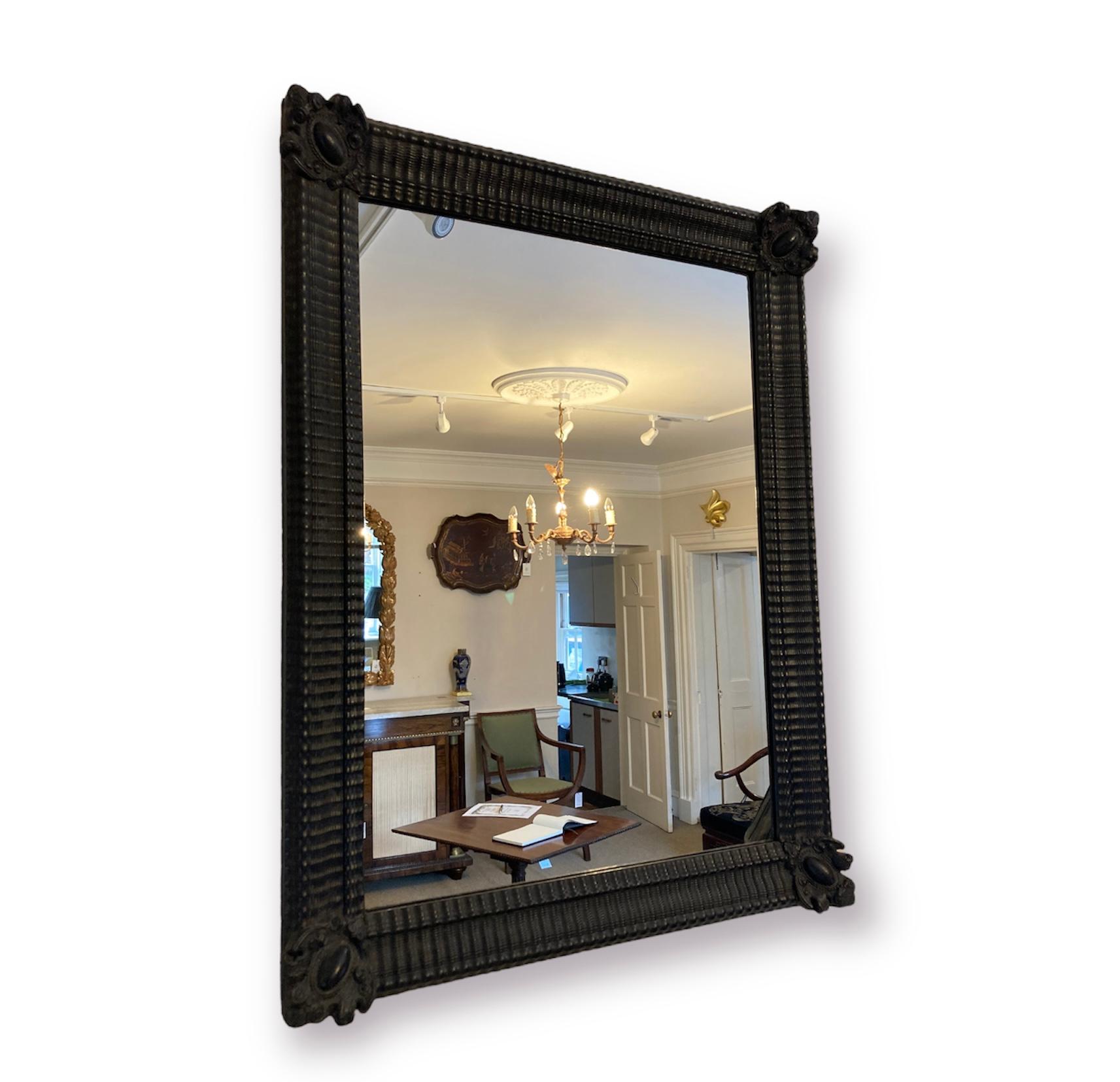 A large Flemish ebonised carved wood ripple frame mirror. A statement mirror in black with detailing to all four corners and moulded ripple effect finished all the way around.
