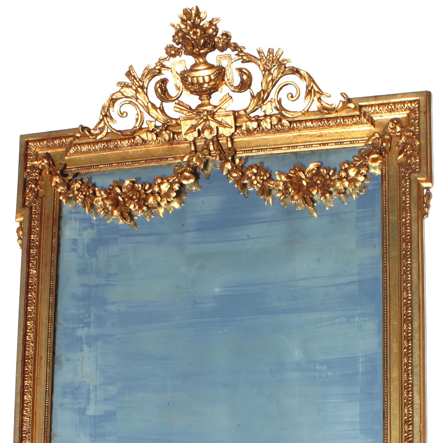 Specchio ornato francese del XIX-XX secolo in stile Luigi XVI in legno dorato e gesso intagliato. La cornice di forma rettangolare è coronata da un'urna floreale fiancheggiata da acanto, volute e foglie, la parte superiore della lastra dello