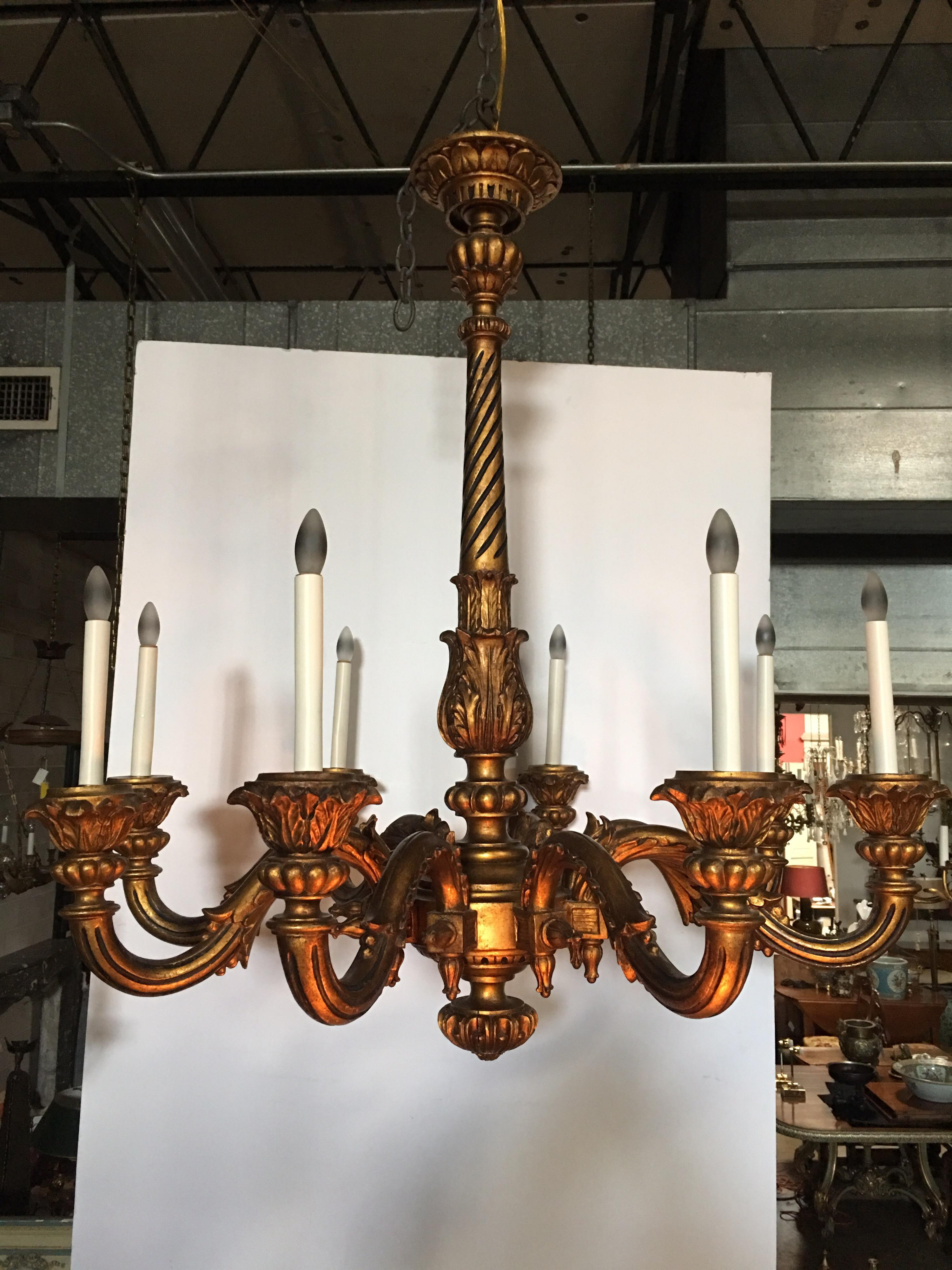 This large antique 19th century French Louis XVI style carved and giltwood chandelier features carved foliate designs, and scrolling branches that end in acanthus leaf bobeches. . The piece has a rich patina throughout.