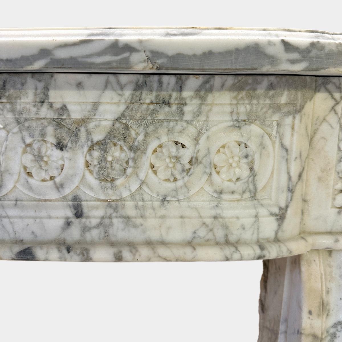 A large 18th century Louis XVI period fireplace, executed i pale and wonderfully veined Calacatta marble. The elegant slim jambs with carved ribbon twist fronts within fluted panels. The bow fronted frieze with running carved Guilloche with carved