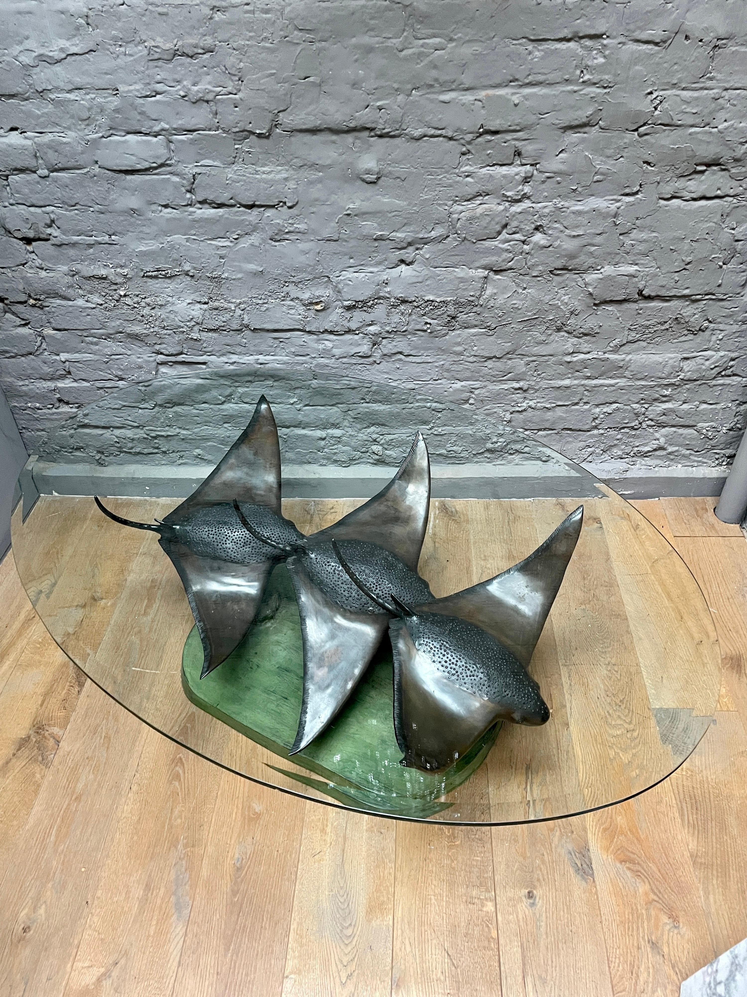 Ein ungewöhnlich großer Bronze-Couch- oder Cocktailtisch mit einer ovalen Glasplatte. Sockel mit Grünspan-Finish auf dem Meeresgrund und drei schwimmenden Stachelrochen aus patinierter Bronze. Sehr gut geworfen und Bewegung einfangend. Am Sockel vom