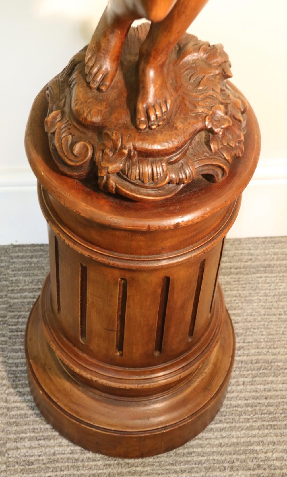 A late 19th century highly decorative large and fine quality carved pine study of a semi-nude mythical boy standing on a fluted pedestal. 
He is holding raised to eye level a large urn which bizarrely has a smiling face which he is in conversation