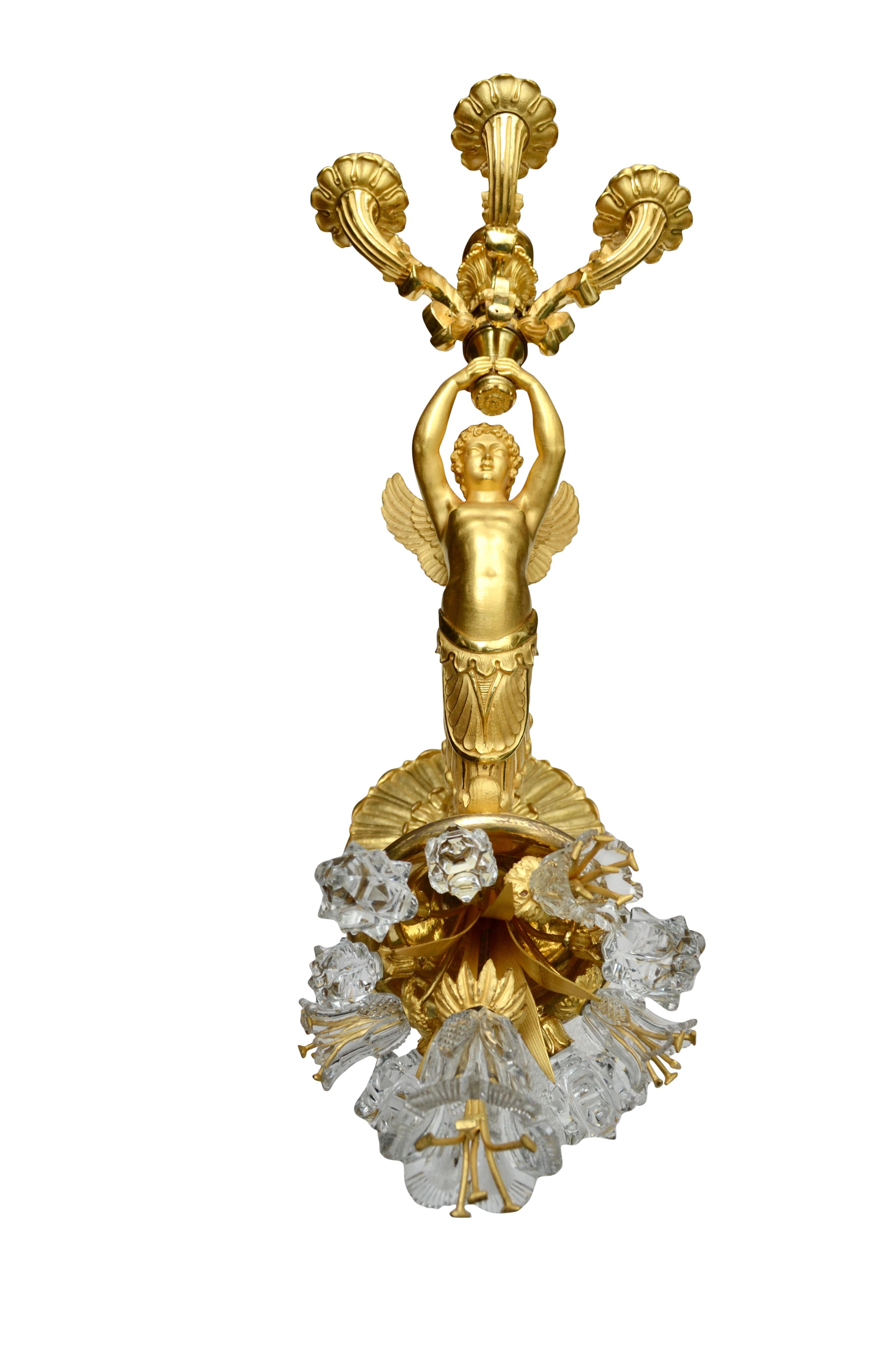 A highly unusual large scale single French Empire wall sconce, the bronze having the finest chasing and gilding ever produced. A winged cupid rides a large cornucopia from which a number of cut crystal flowers and stems germinate. The elaborate