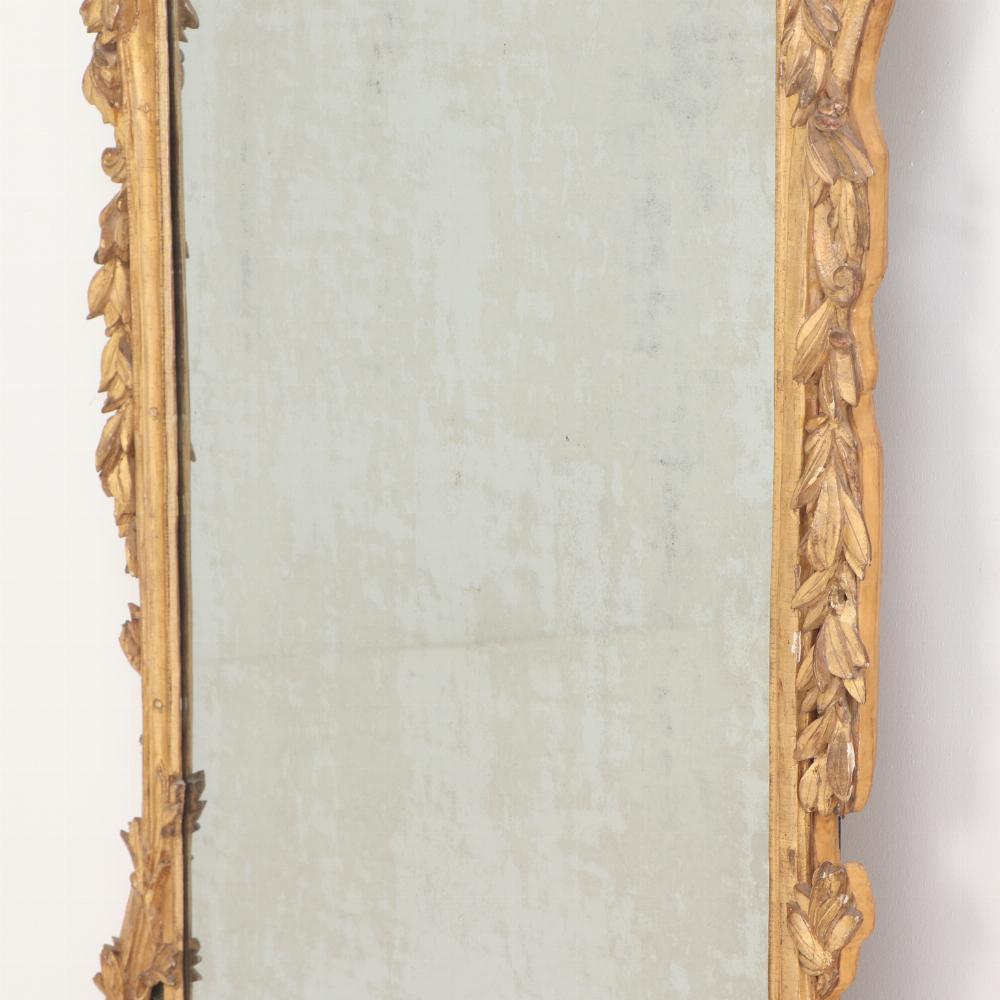 Splendidamente intagliato, questo specchio in legno dorato è ricco di dettagli. Un getto floreale intagliato all'interno di uno stemma circolare si trova in cima alla cornice rettangolare. L'intera cornice è intagliata con ulteriori ornamenti