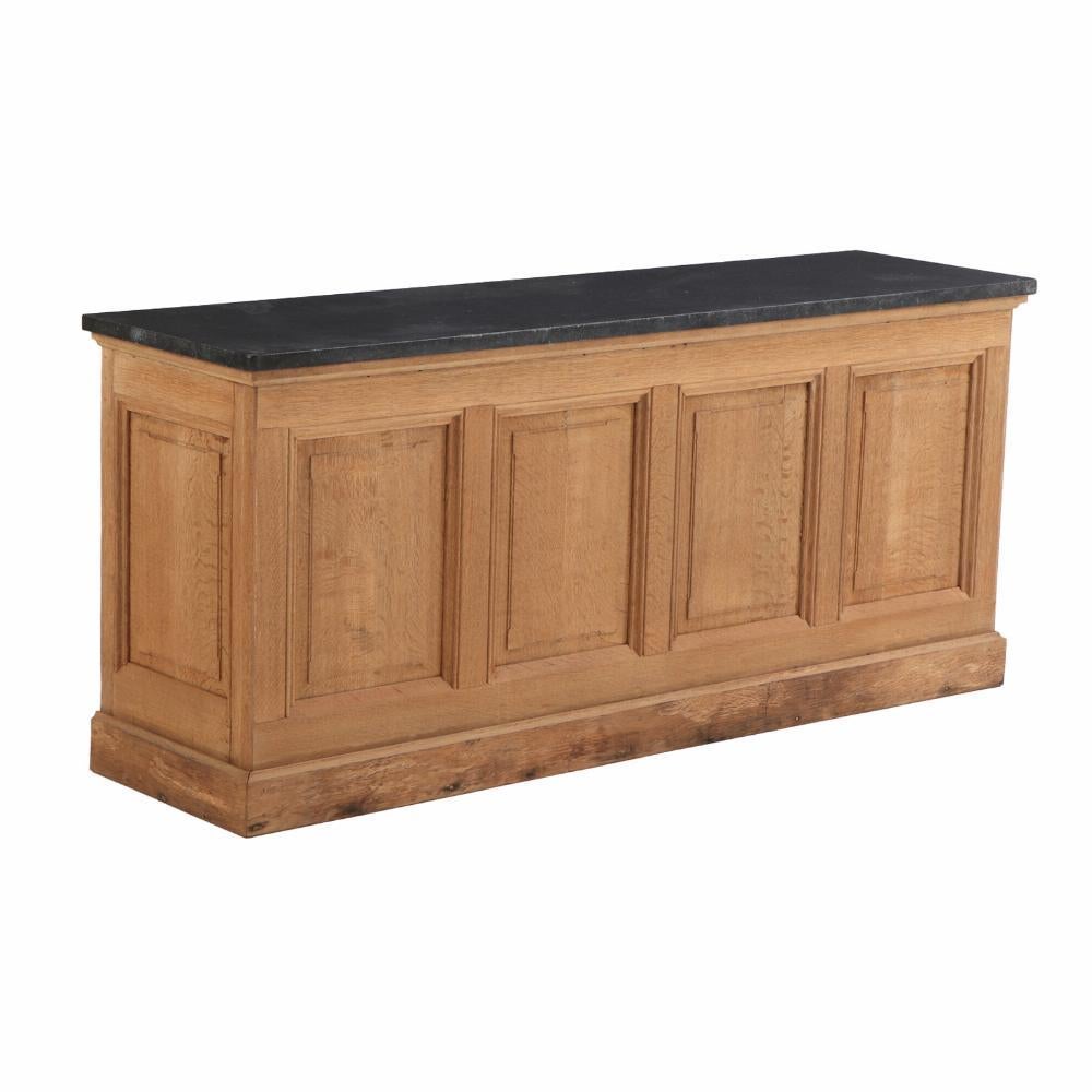 Un imponente e ben proporzionato bancone da negozio francese del 1900 circa, realizzato in rovere massiccio con una ricca patina e i classici dettagli dei pannelli in rilievo. Il piano è dotato di un'importante lastra di pietra blu belga, apprezzata