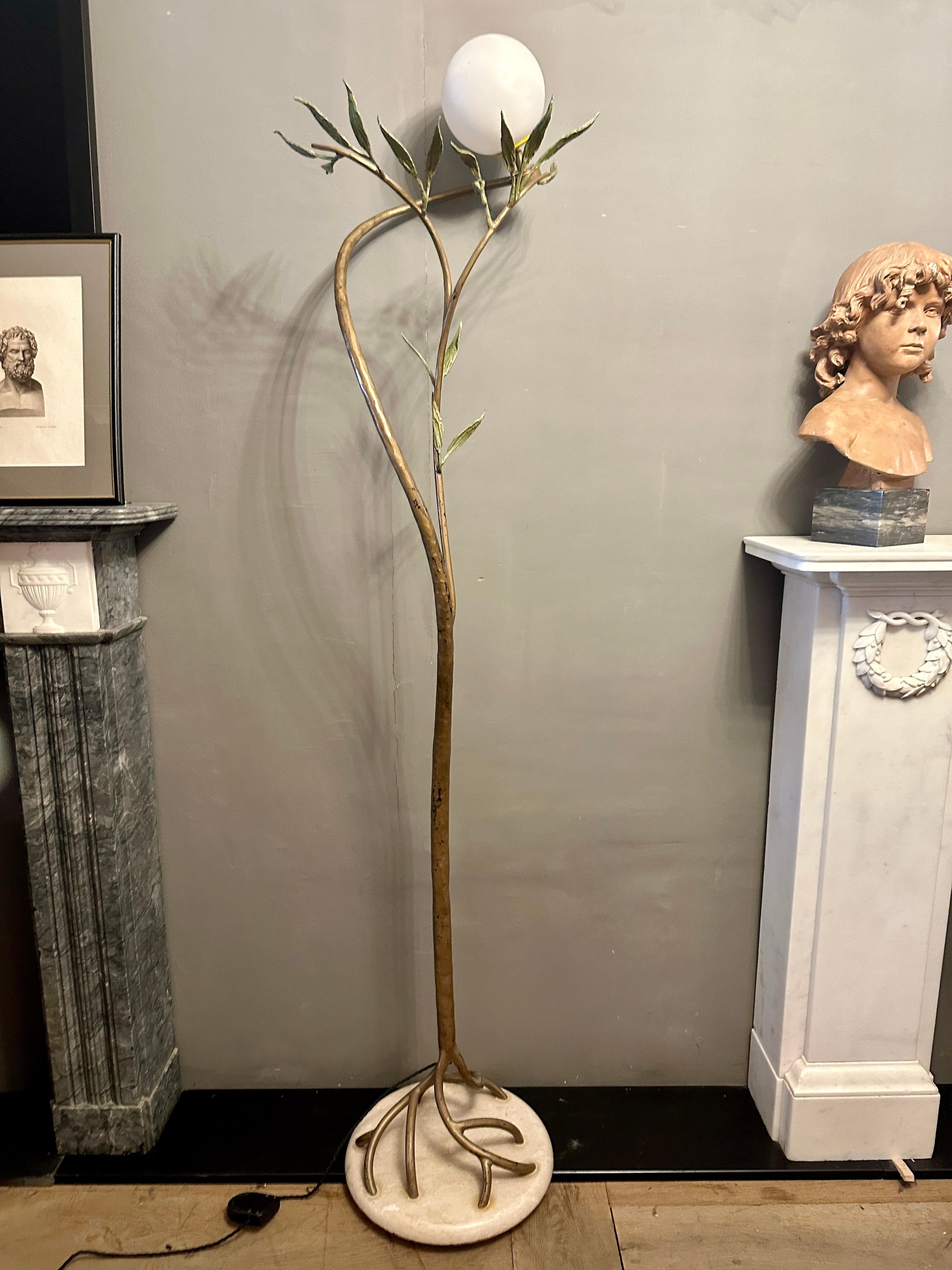 Lámpara de pie grande y muy alta, de hierro forjado y pintado, de forma foliada, con pantalla de esfera blanca sobre un accesorio pivotante. La base es de travertino italiano pulido, con tallo patinado en bronce y hojas pintadas de verde. 
Lámpara