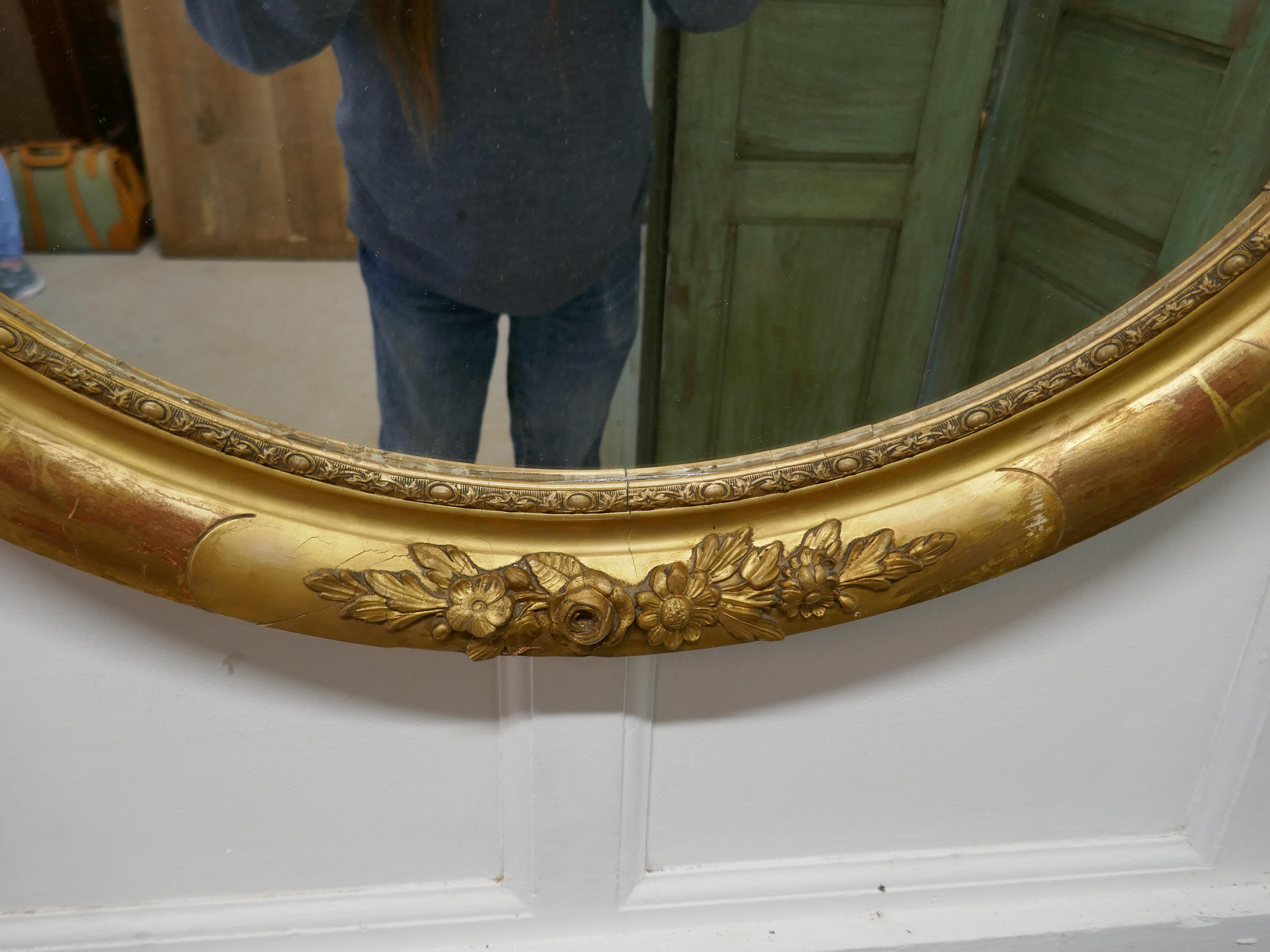 A large French Rococo oval gilt wall mirror

The mirror has a very attractive 3.5” wide gilt frame in the Rococo style, it is decorated with many flowers. In the border the red oxide undercoat is peeping through giving the piece a luxurious if