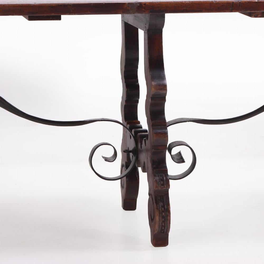 La parte superior, larga y rectangular, descansa sobre tres soportes en forma de lira y caballete perfilado, con camillas de hierro con volutas. Una magnífica mesa de comedor, pero también podría ser una mesa de sofá detrás de un gran sofá, dado el