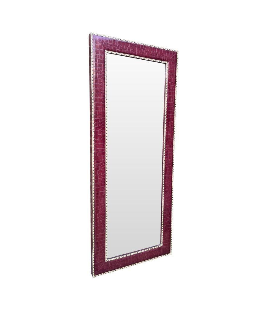 A large contemporary full length mirror with burgundy faux crocodile skin frame with brass studded details