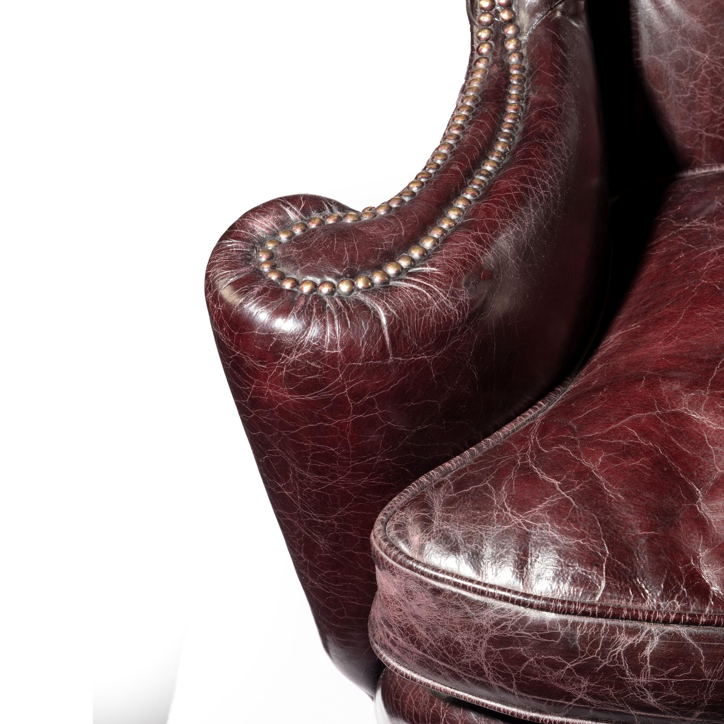 A large George I style burgundy leather wing armchair, of typical shape and generous proportions with pepper-box arms set above cabriole front legs with scroll spandrels and outswept back legs. Reupholstered in distressed deep buttoned burgundy