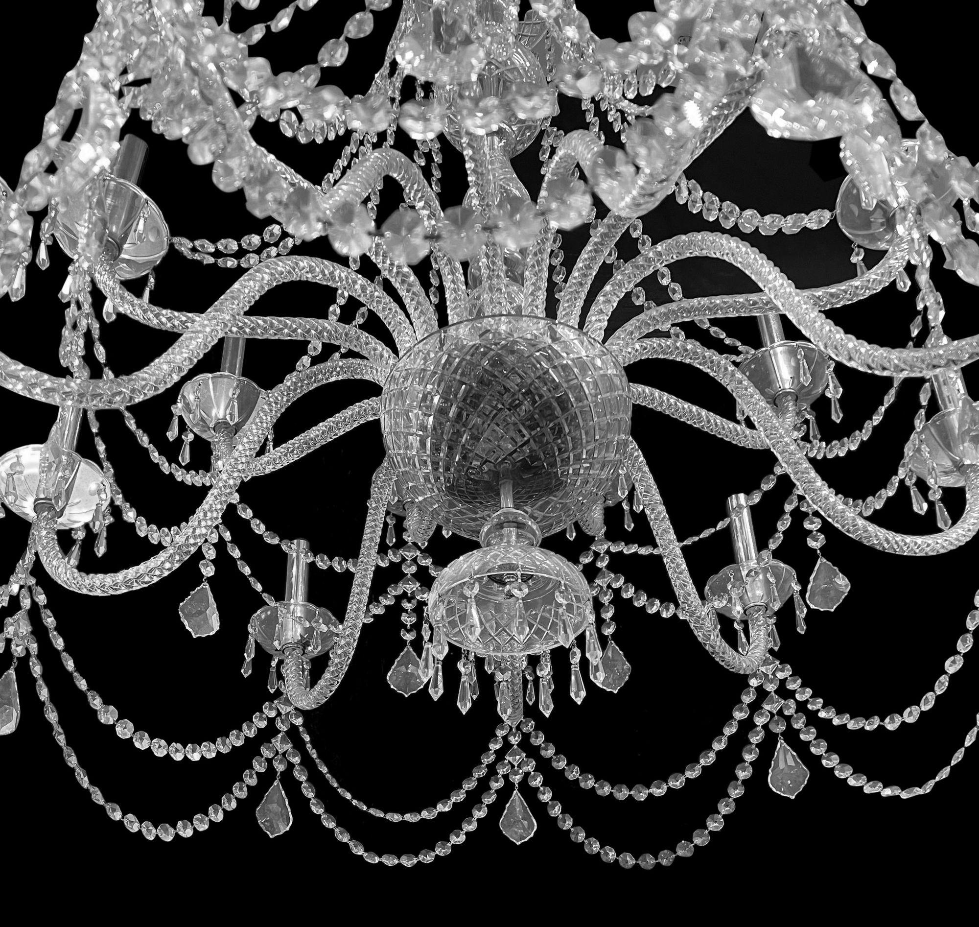 A very impressive George III style cut glass 20 branch chandelier. 
The shaped glass bowl issuing spiral rods suspending faceted drops, swags and chains above a slender baluster stem and bowl, issuing two tiers of twenty S-scrolled spiral cut arms