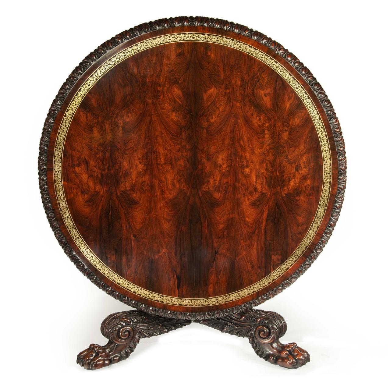 The circular tilt top has a central field of book-matched, figured rosewood within a broad band of cut brass inlay.  The edge is boldly carved with an acanthus and dart border.  The central support is hexagonal in section with a broad central