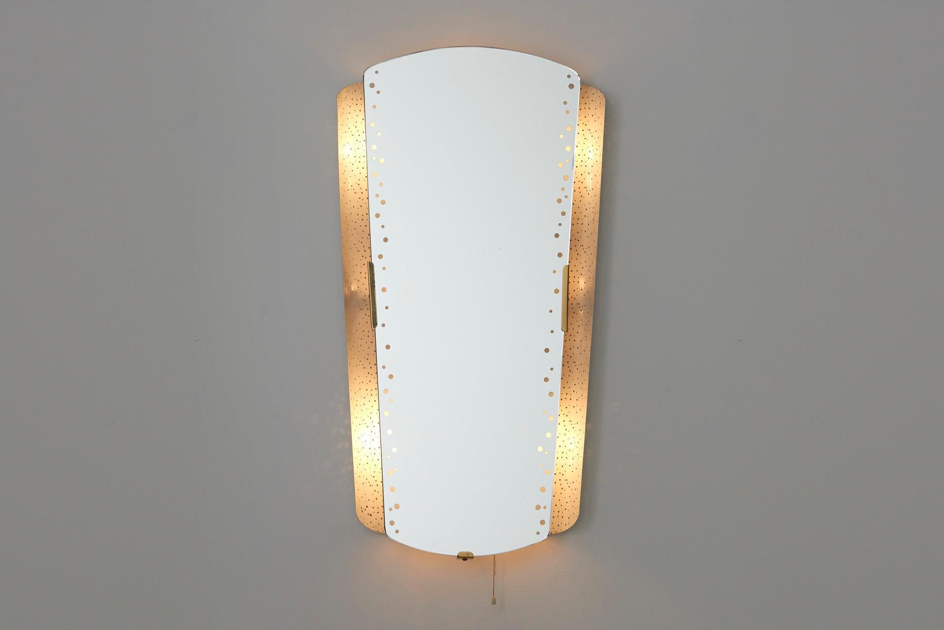 A large backlit mirror, held by brass brackets. The light is reflected by a curved perforated plate, and shines through the dots in the mirror. Designed in the 1950s by Ernest Igl and made by Hillebrand Leuchten in Germany. The mirror holds 6 E27