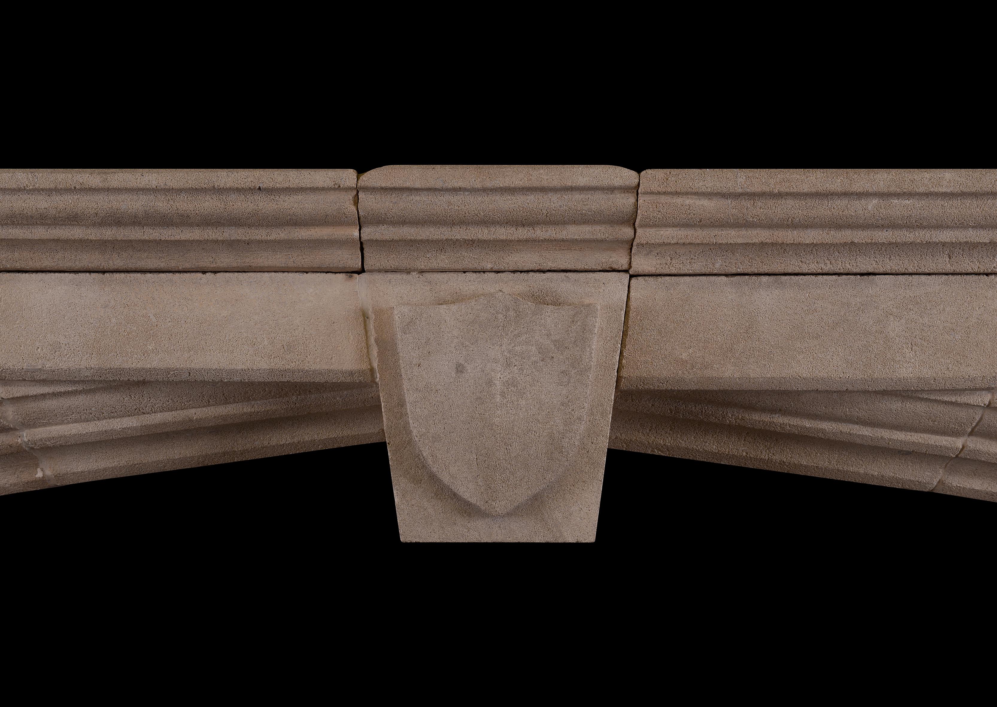 A large and imposing bath stone fireplace in the Gothic manner. The moulded jambs surmounted by arched frieze with keystone featuring shield to centre. Moulded shelf about. English, circa 1900. Overall width could be reduced to around 2000mm if