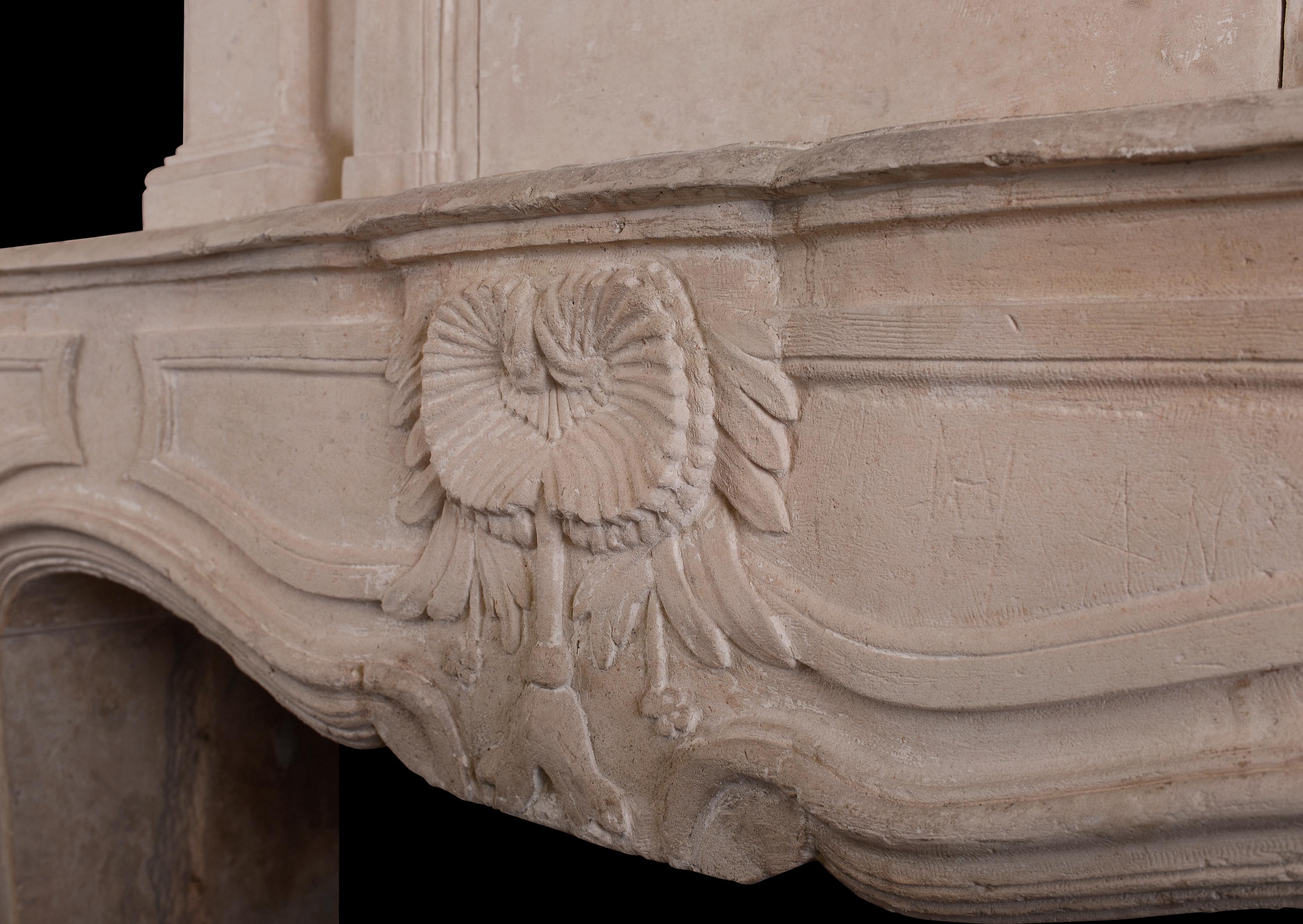 A large and impressive French limestone trumeau fireplace. The panelled jambs surmounted by shaped, panelled frieze with carved foliage to centre. The overmantel with panel moulding to centre flanked by carved scrollwork. Moulded top shelf above.