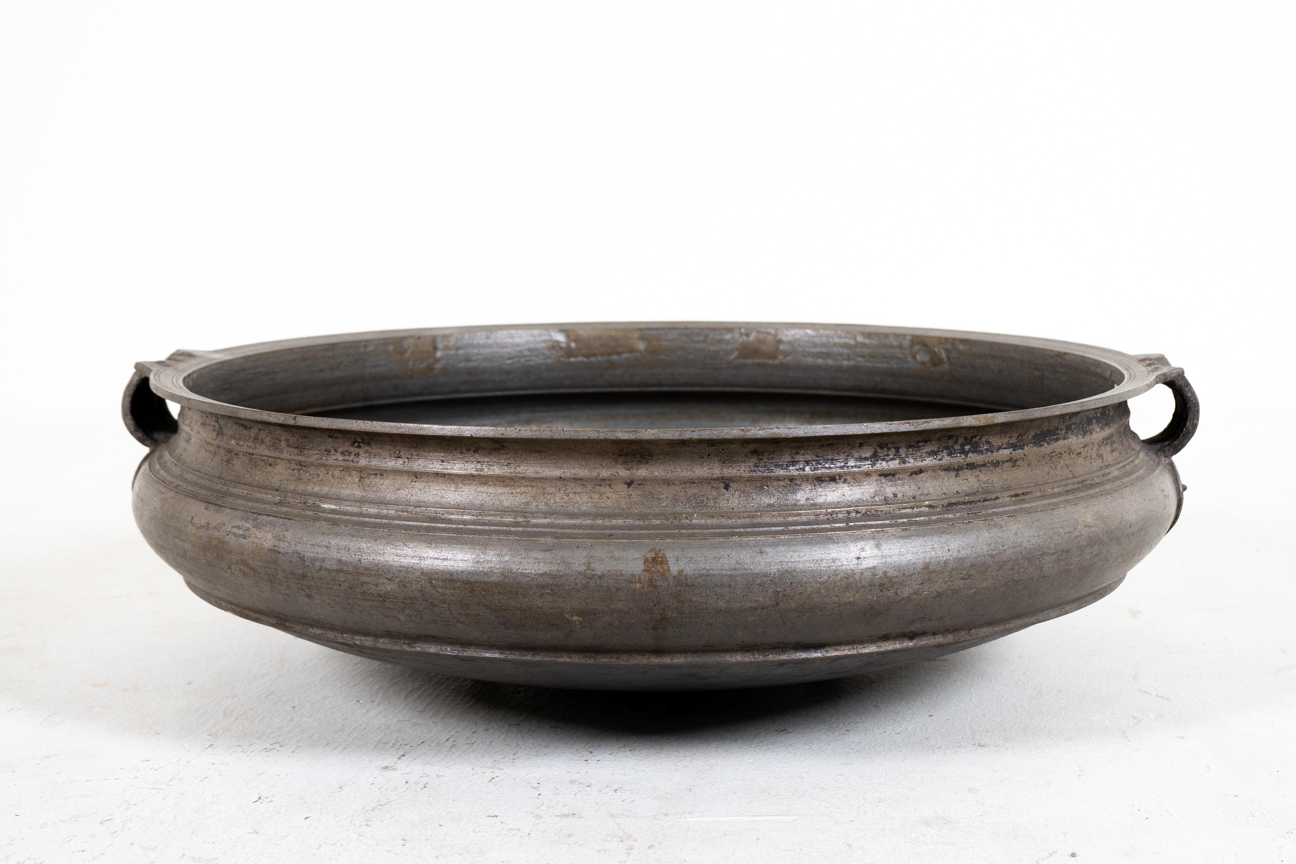 This shallow bronze bowl is an open fire cooking vessel known as urli or uruli, used throughout southern India for preparing ayurvedic medicines and cooking large quantities of food for gatherings and ritual offerings. Cast of bell bronze using the