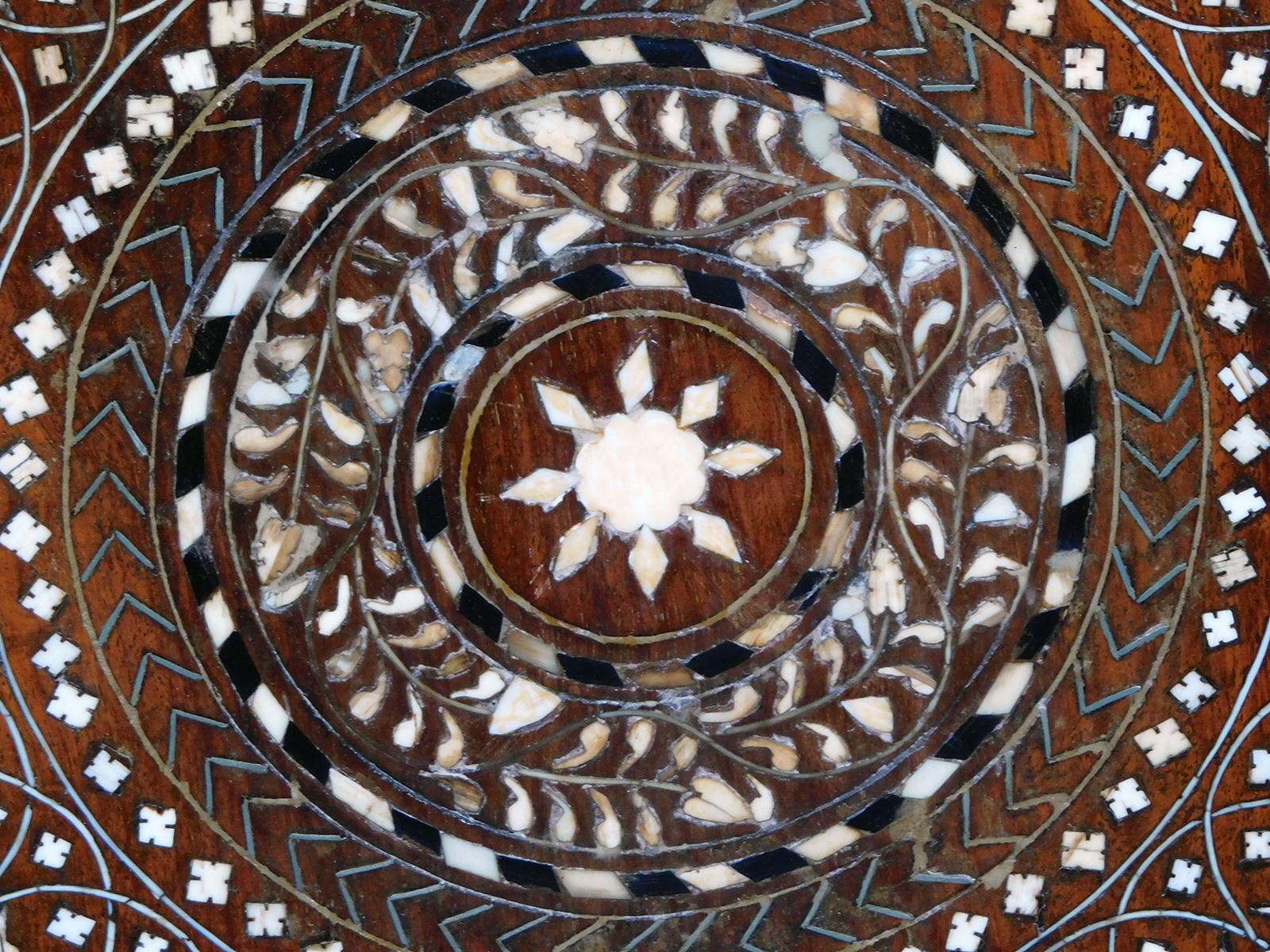 Originally used as traveling tea tables for the British in India; the octagonal top with central medallion surrounded stylized foliate designs within a border of meandering vines; raised on a hinged base with arabesque spandrels.