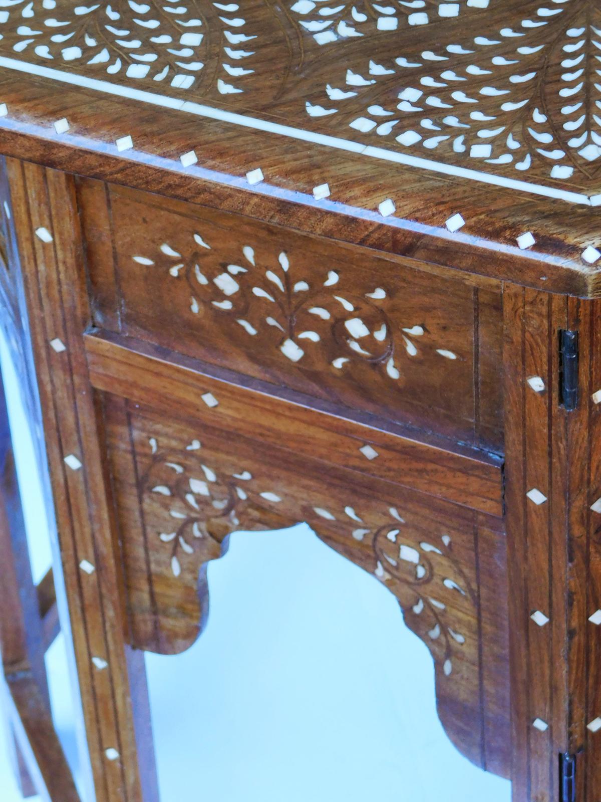 Originally used as traveling tea tables for the British in India; the octagonal top with central medallion surrounded stylized foliate designs within a border of meandering vines; raised on a hinged base with arabesque spandrels.