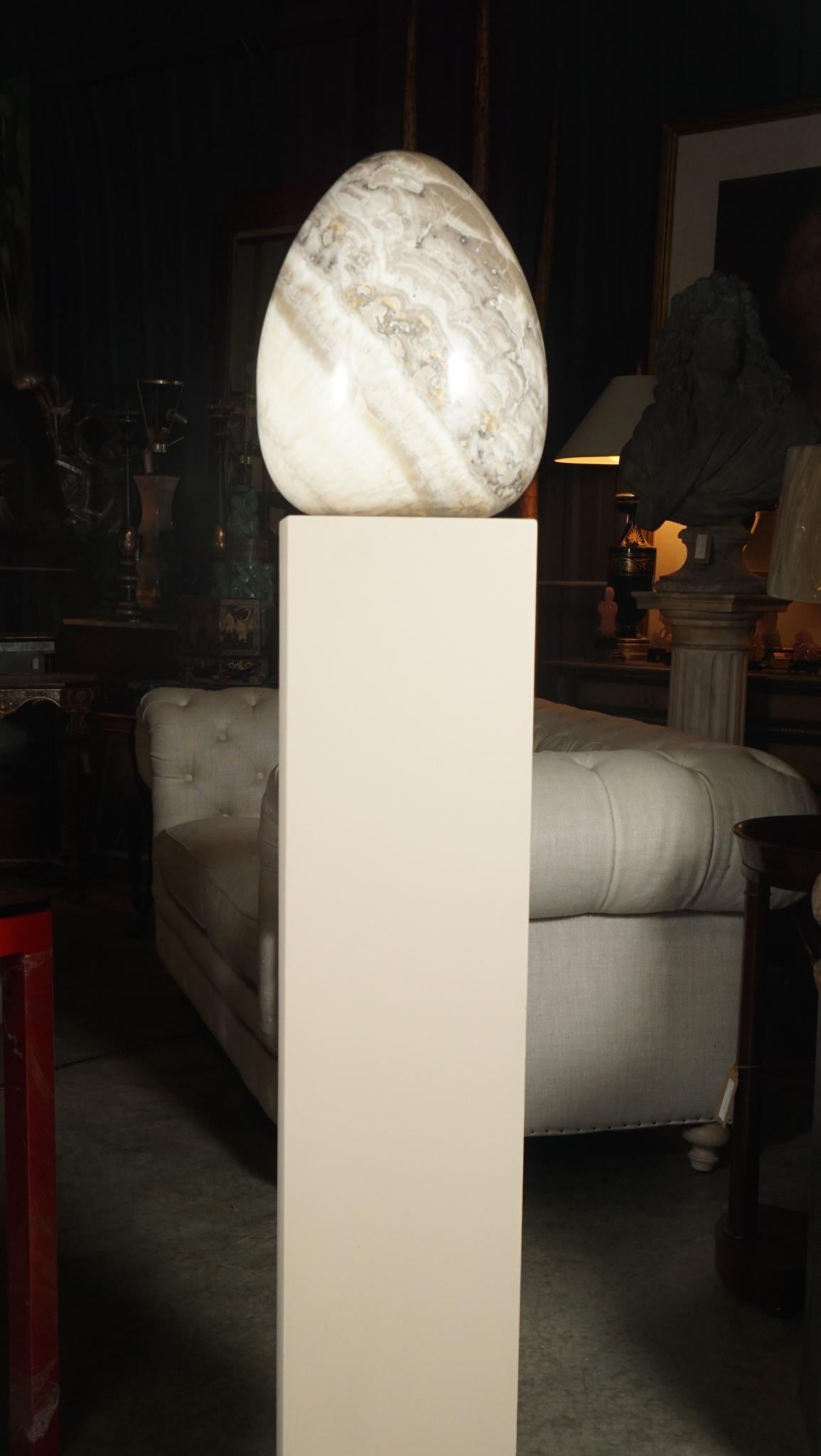 Sculpté dans un seul bloc d'onyx rare, ce grand œuf sculpté repose sur un piédestal électrifié qui crée une lumière interne pour l'œuf, lui donnant une forme géométrique lumineuse. La lumière éclaire le matériau, ce qui permet au spectateur de voir