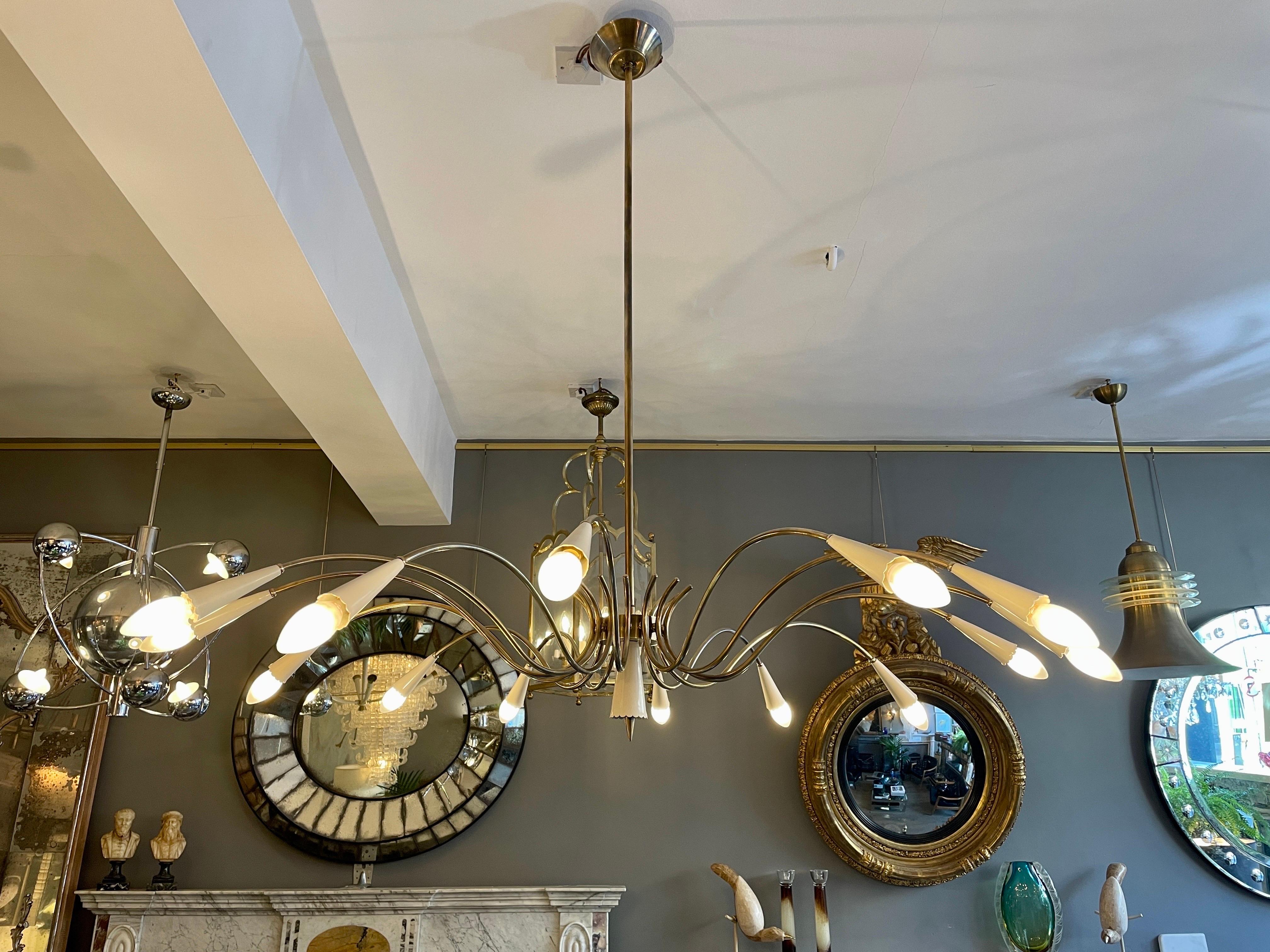 A large Italian Spider chandelier in patinated brass and Ivory white lacquer. Expertly restored to its original design. With original ceiling rose, long brass stem supporting the central fitting with scrolled sweeping arms terminating in con shaped