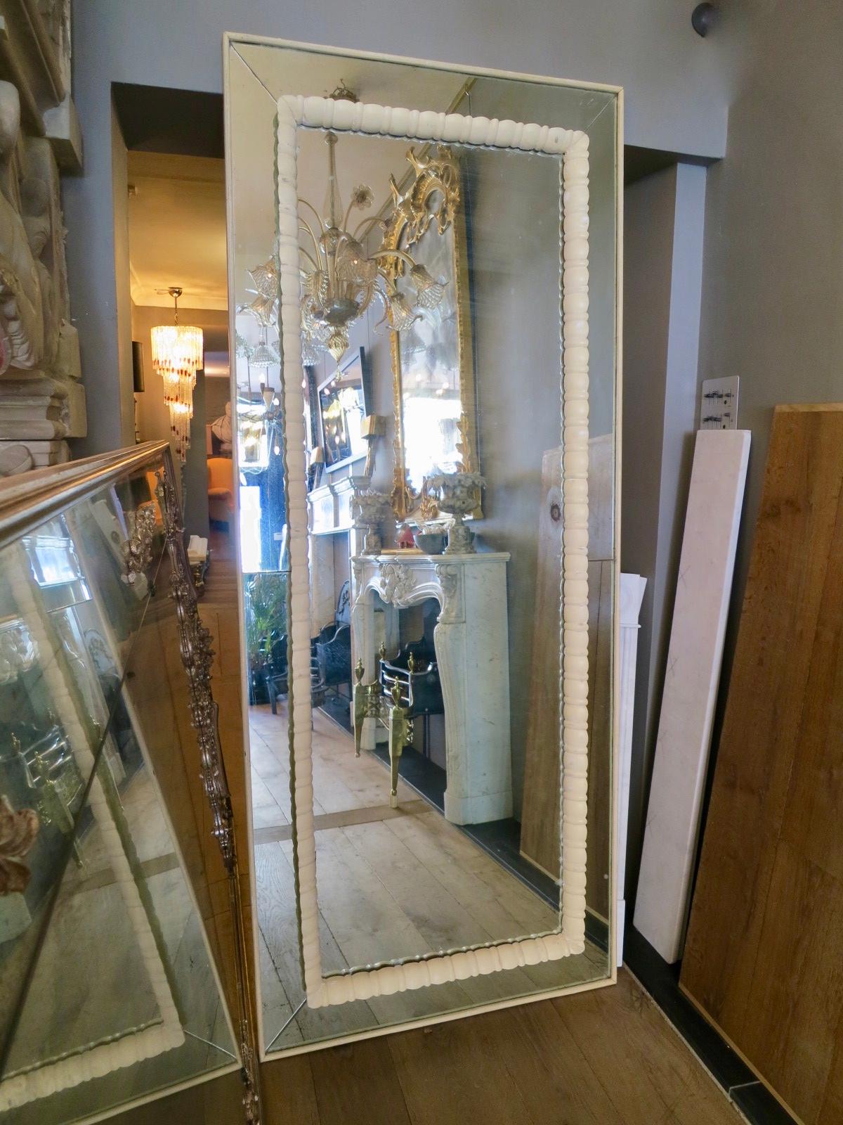 Grand miroir italien à panneaux dans un cadre blanc vieilli avec une bordure décorative à l'intérieur. Le miroir a une vague teinte verte, avec quelques zones de rousseur dénotant l'âge. Peut être accroché à l'horizontale, à la verticale ou au sol.