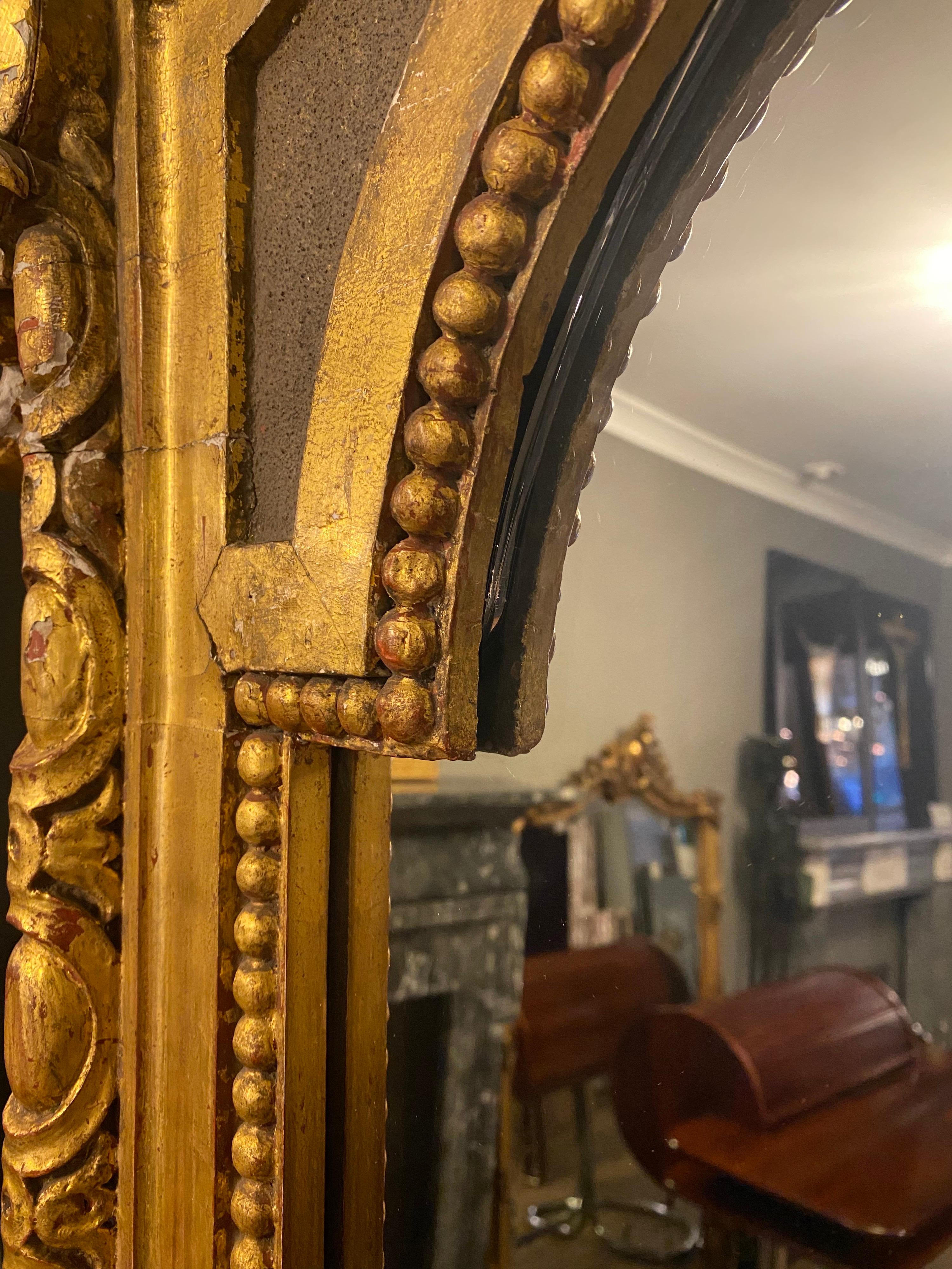 A very large gold gilt carved wood mirror, decorated with a large shell pediment, scrolled acanthus leaf, and foliate details. An egg and dart frame with beaded inner slip. Original wear and patina and some carving lost over the years, all shown in