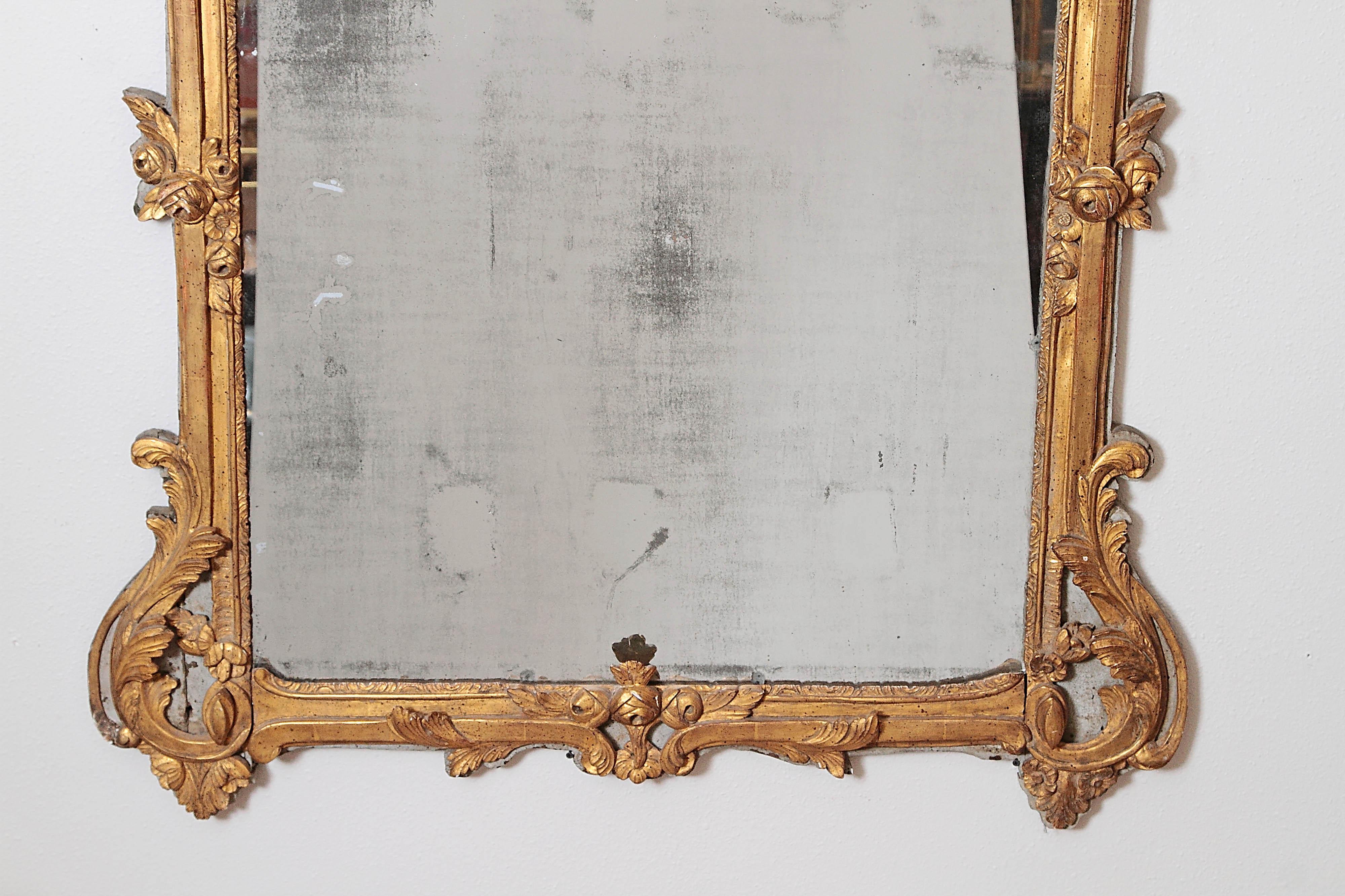 A large Louis XV style hand carved, painted and gilded mirror having its original gilding over carved wood with a French grey painted background, retaining its original two-part mirror plate. Likely region of Provence.