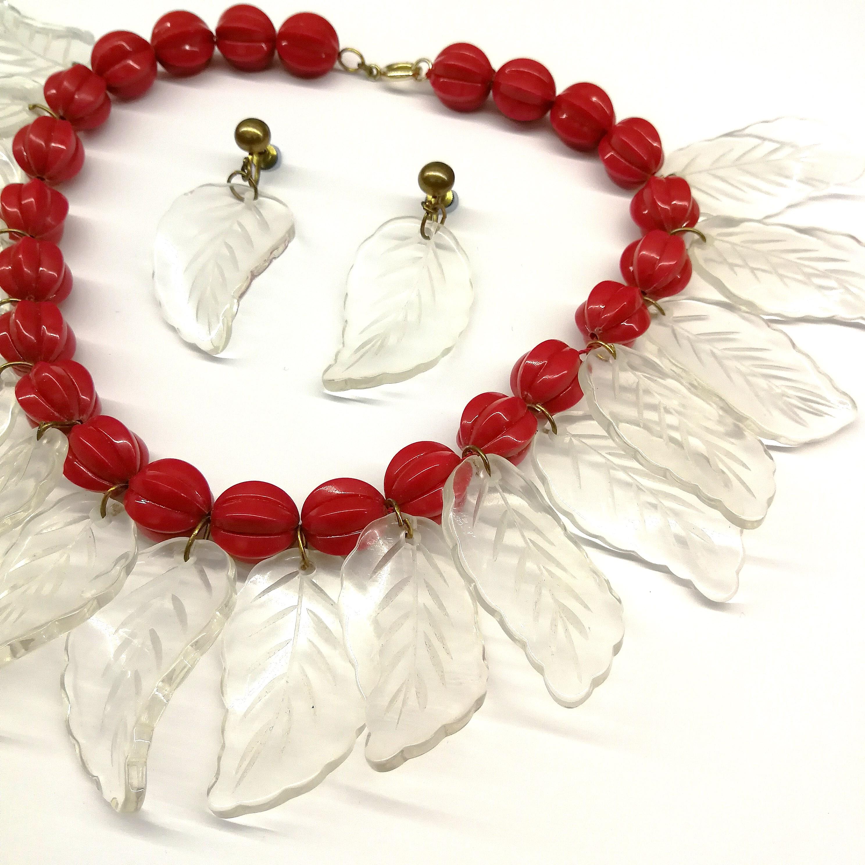 A striking and impressive carved Lucite necklace, with matching drop earrings, from the 1940s ,that has clear 'leaves' hanging down around the necklace, and from each earring, with carved red ball motifs making up the necklace itself. Light to wear,