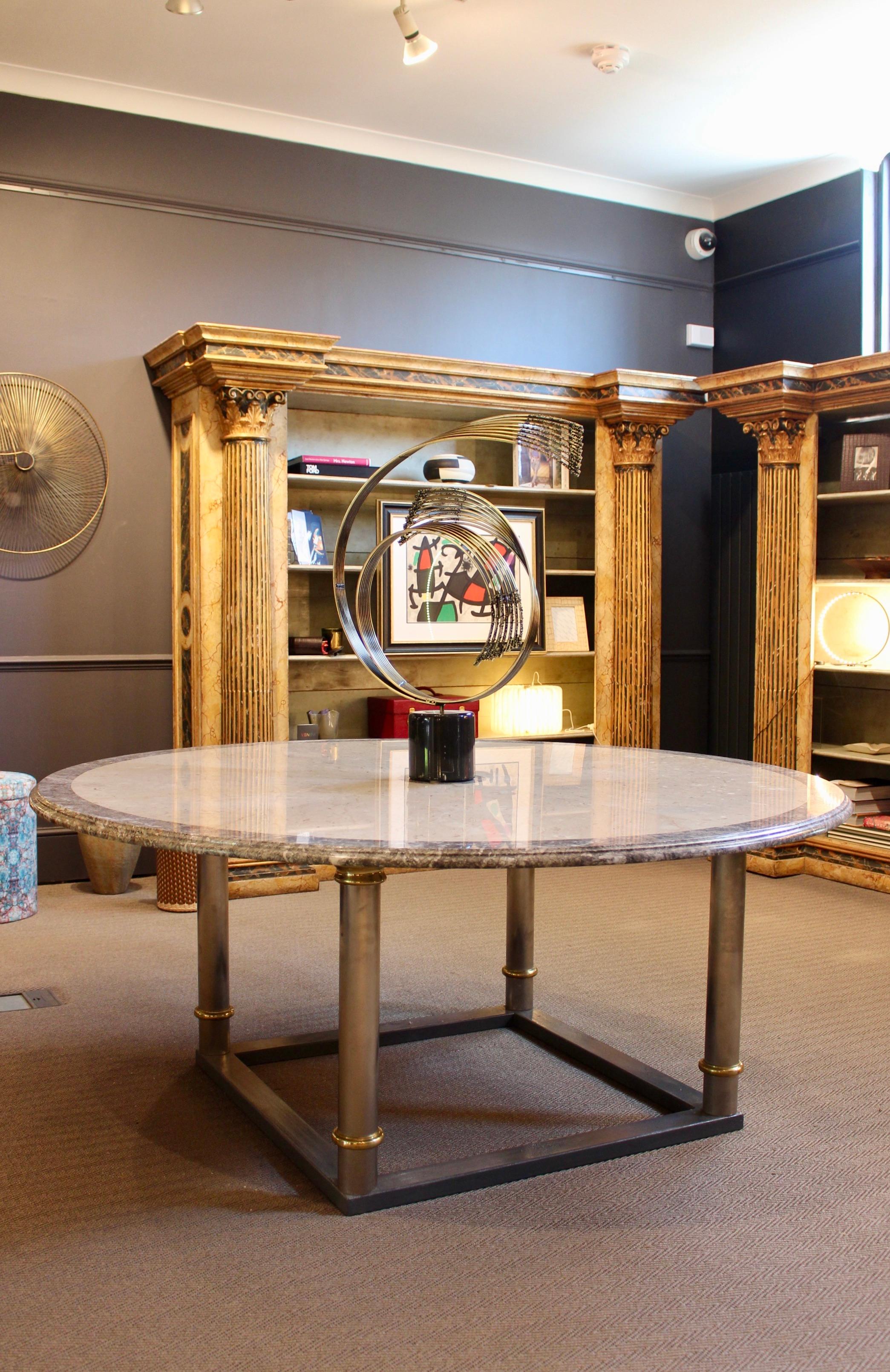 A Large Marble Top Circular Table, circa 1980. The segmental fossilised marble veneer with darker outer band and central circle, on brass and steel circular base