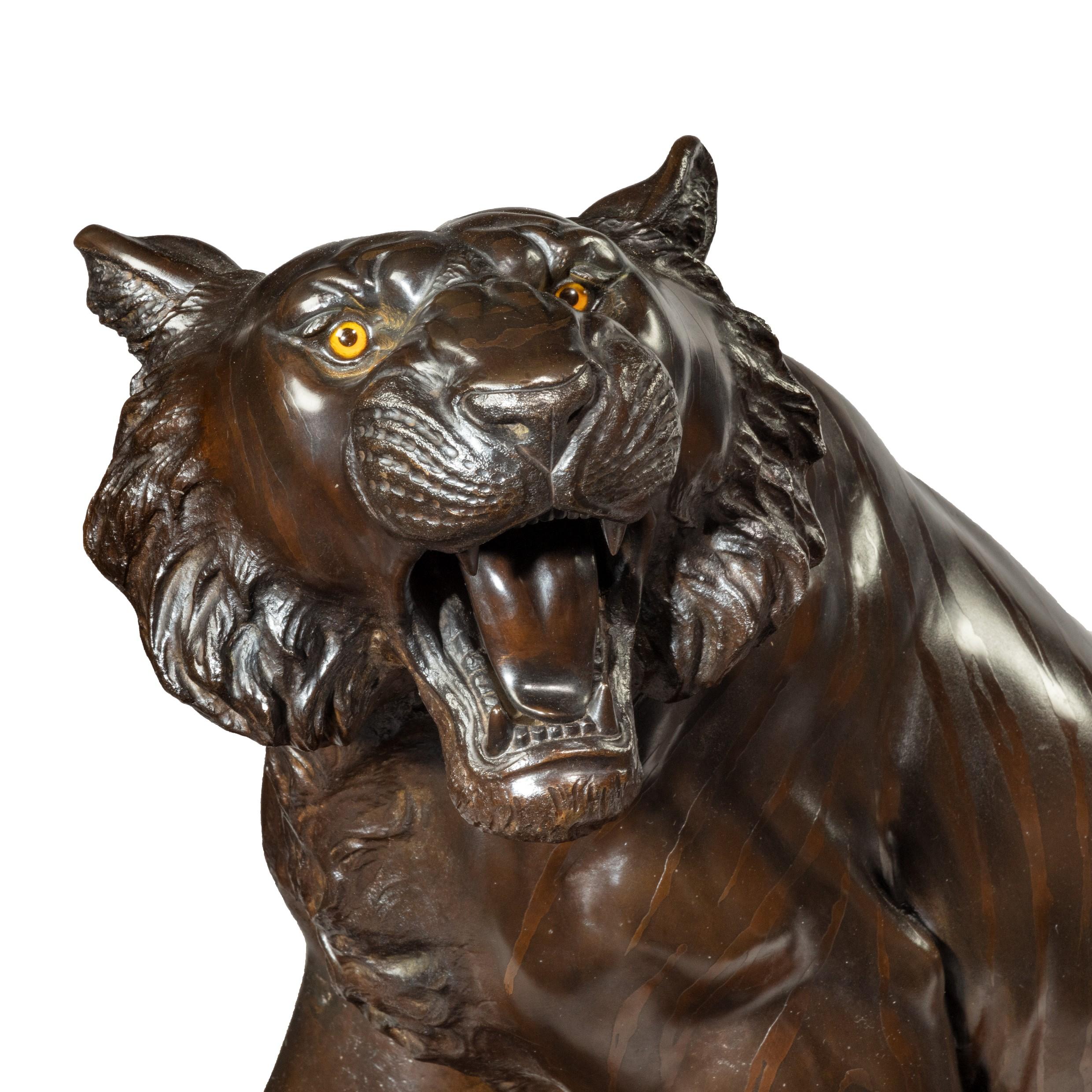 Large Meiji period bronze tiger by Genryusai Seiya, striding forward with teeth bared, the bronze patinated to imitate tiger stripes, with inlaid glass eyes, set on a gnarled rootwood base. Impressed seal mark Dai-Nihon Genryusai Seiya zo [Made by